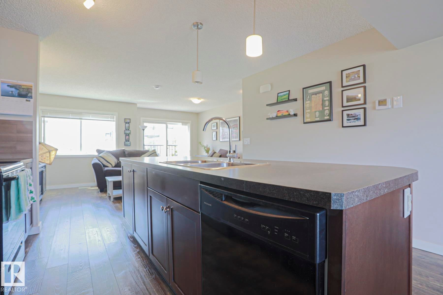 Kitchen island featuring dark wood-finish cabinetry, quartz countertops, and an integrated black dishwasher - 1622 33A Street Nw, Edmonton, AB - Indoor Photo Showing Kitchen With Double Sink