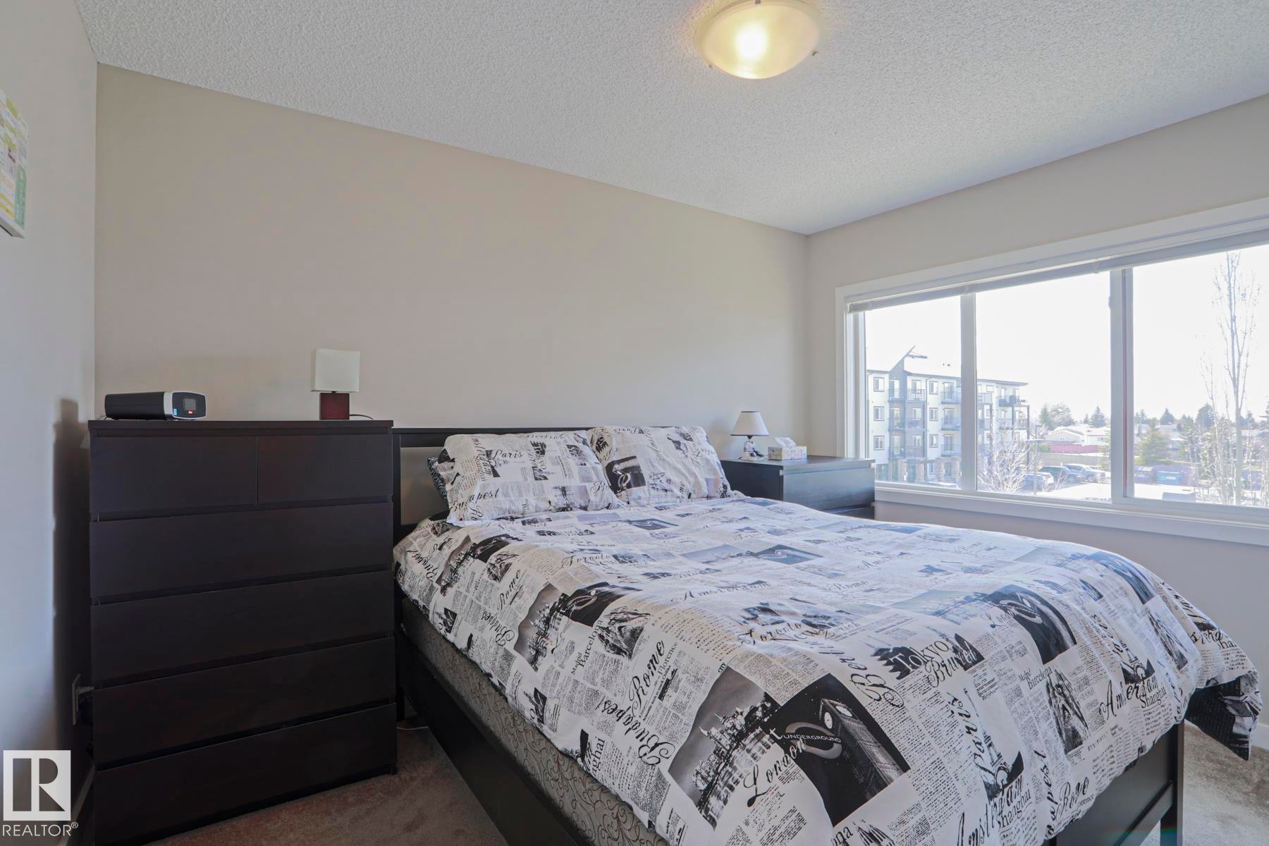 Master Bedroom featuring neutral wall paint, textured ceiling, a large window with white trim, and carpet flooring - 1622 33A Street Nw, Edmonton, AB - Indoor Photo Showing Bedroom