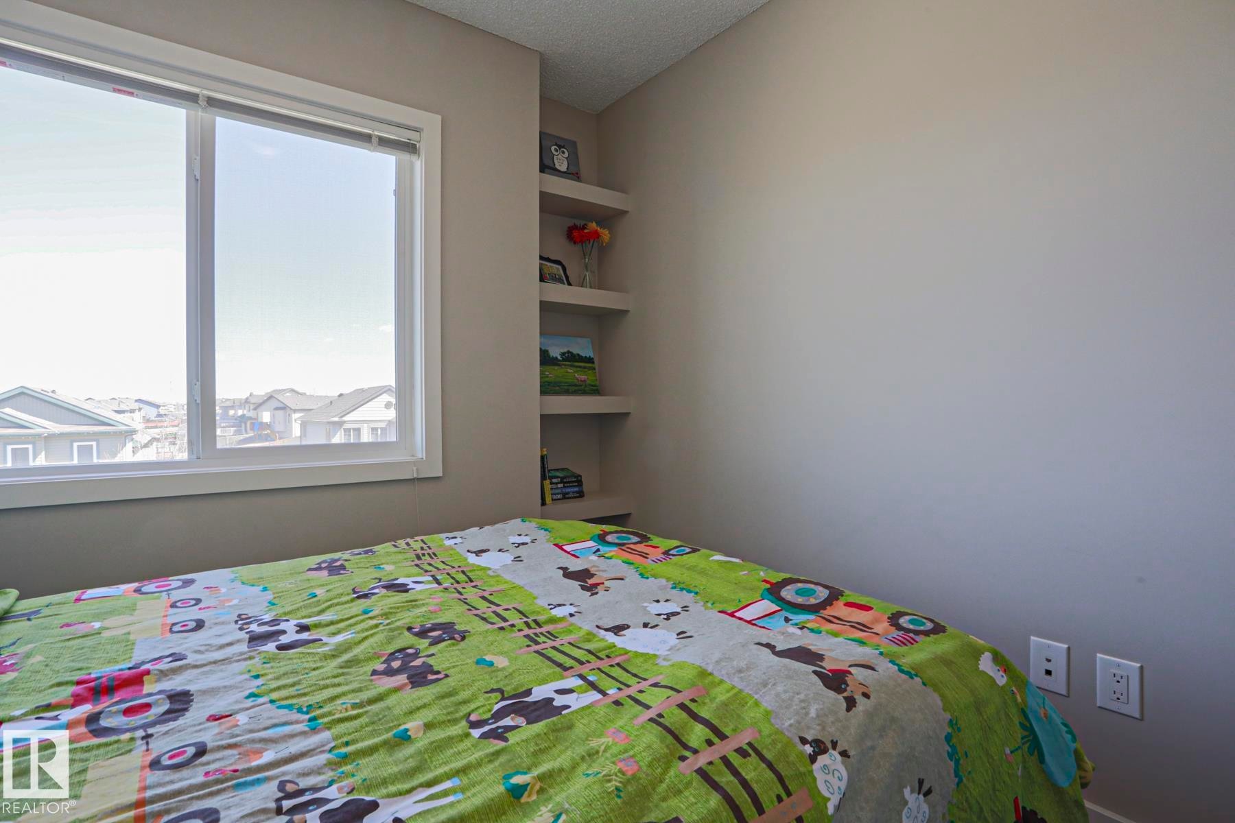 2nd Bedroom with built-in corner shelving, a large window, neutral wall tones, and white trim - 1622 33A Street Nw, Edmonton, AB - Indoor Photo Showing Bedroom