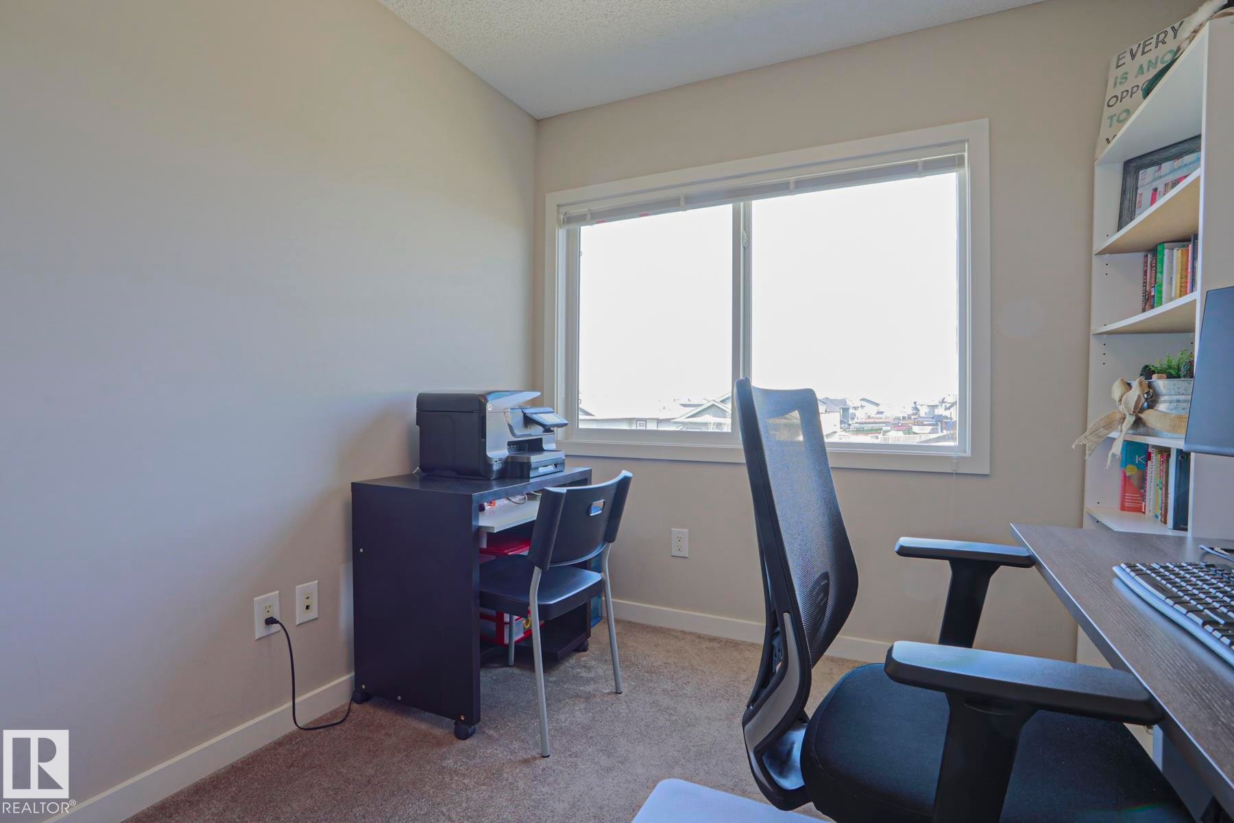 Bright interior room featuring a large window with white trim, neutral wall color, and carpeted flooring - 1622 33A Street Nw, Edmonton, AB - Indoor Photo Showing Office