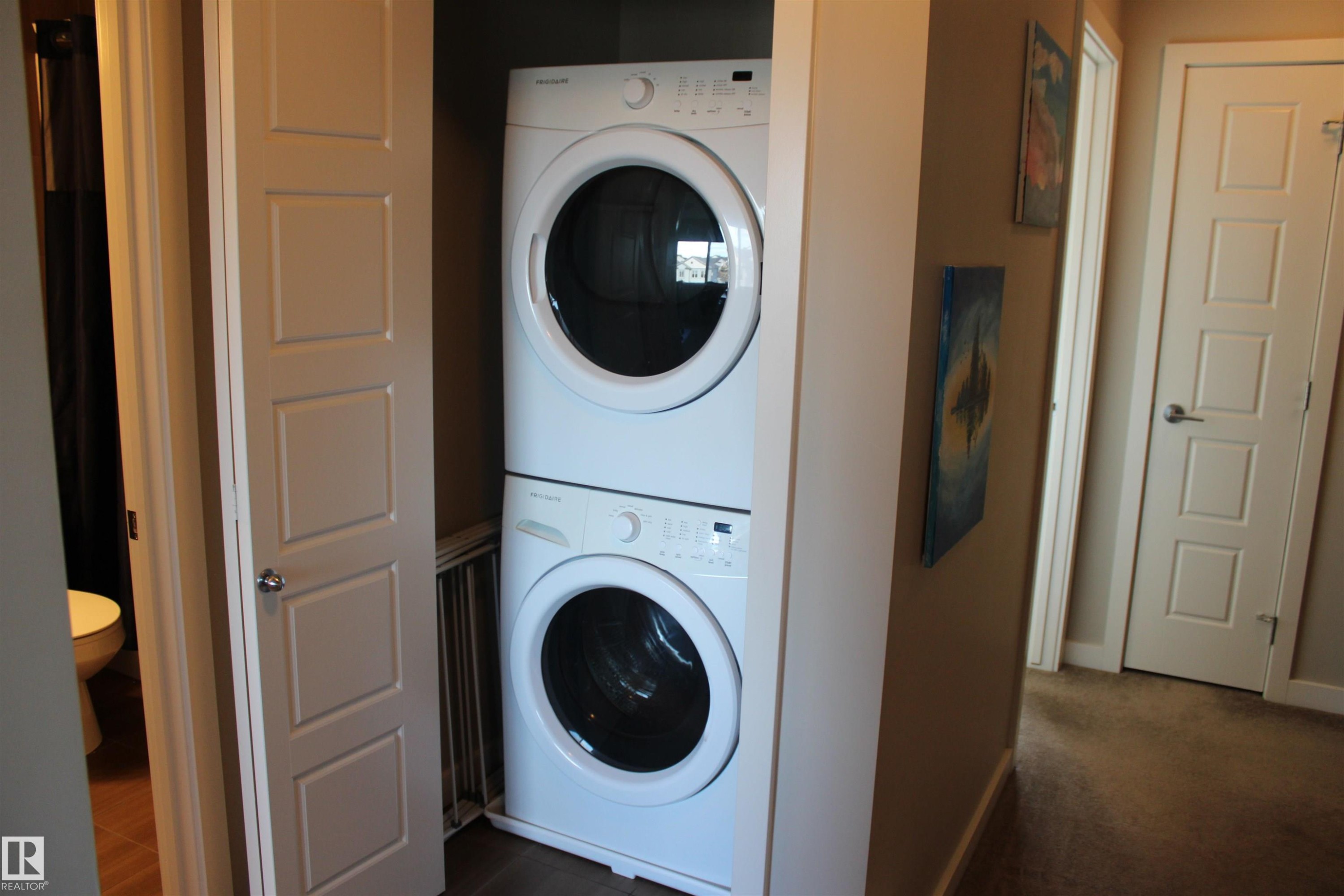 Stackable washer and dryer appliances within a dedicated closet space, featuring a louvered vent and adjacent paneled doors - 1622 33A Street Nw, Edmonton, AB - Indoor Photo Showing Laundry Room