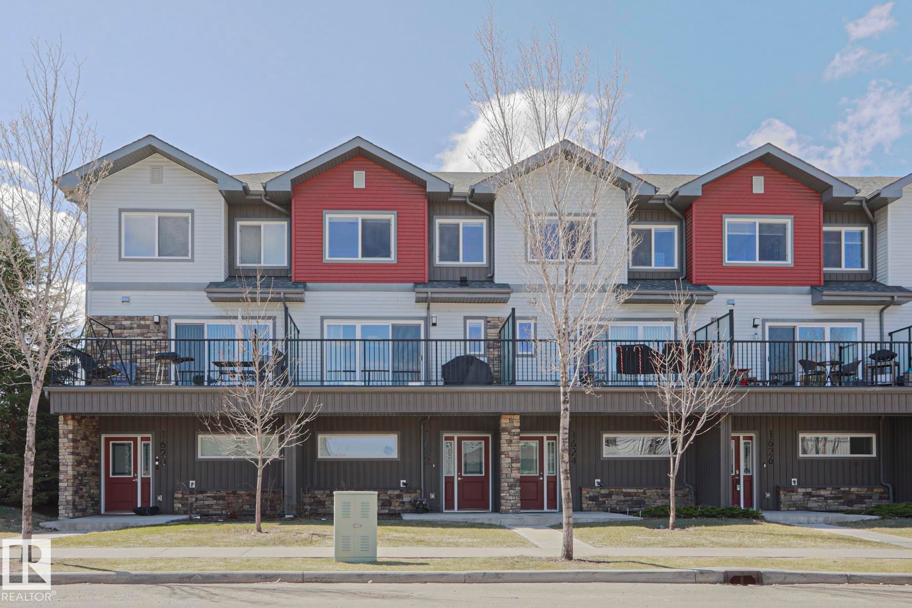 Multi-level townhome exterior featuring red and white siding accents and stone veneer detailing Very well built attractive homes. - 1622 33A Street Nw, Edmonton, AB - Outdoor With Balcony With Facade