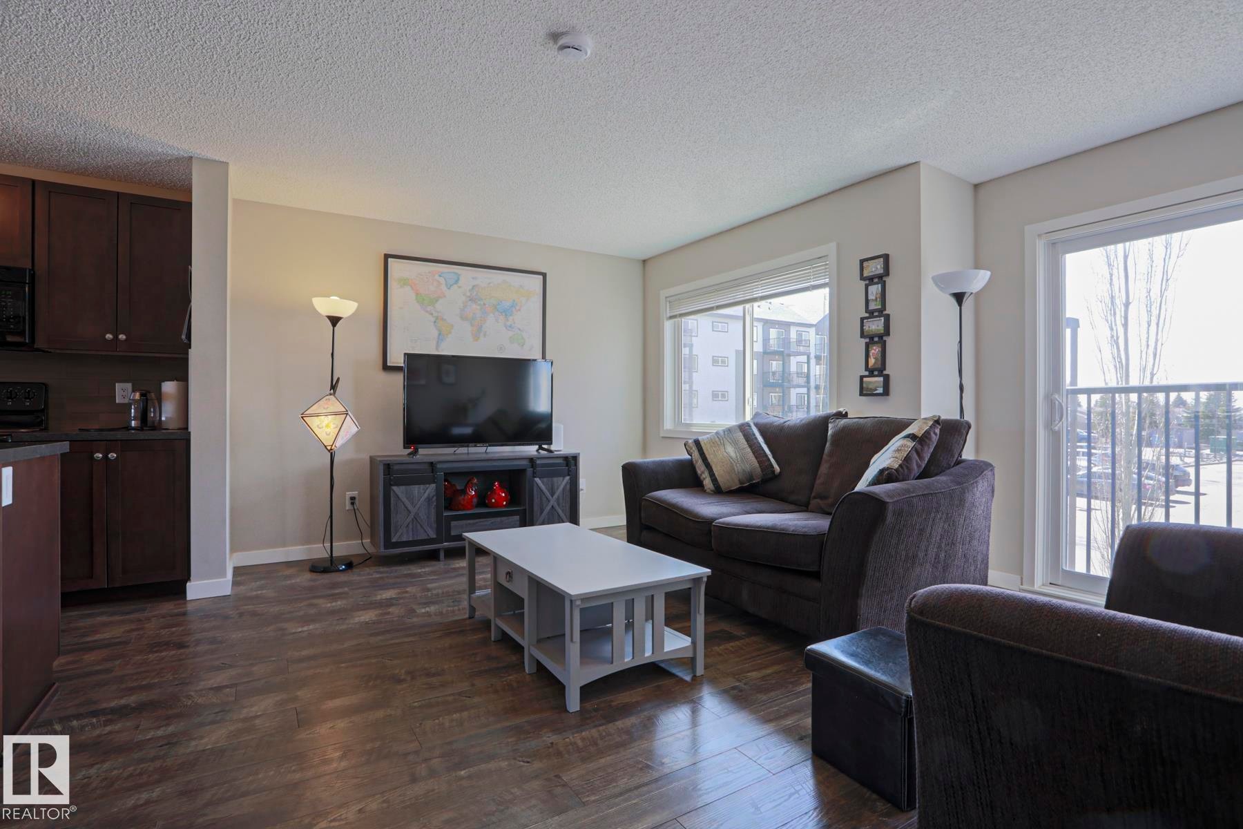 Spacious living area featuring laminate flooring, light-toned wall paint, and a large windows with a Juliette sliding door balcony - 1622 33A Street Nw, Edmonton, AB - Indoor Photo Showing Living Room