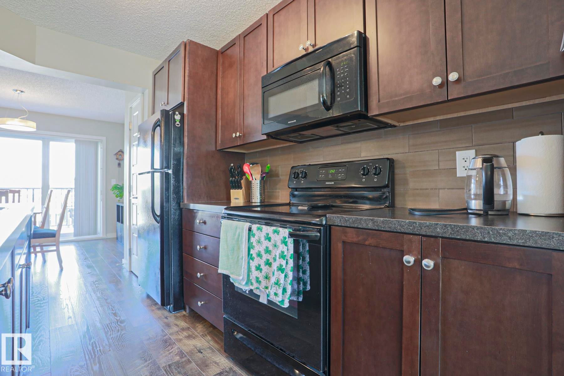 Kitchen featuring rich wood-finish cabinetry, black appliances, and a tiled backsplash - 1622 33A Street Nw, Edmonton, AB - Indoor Photo Showing Kitchen