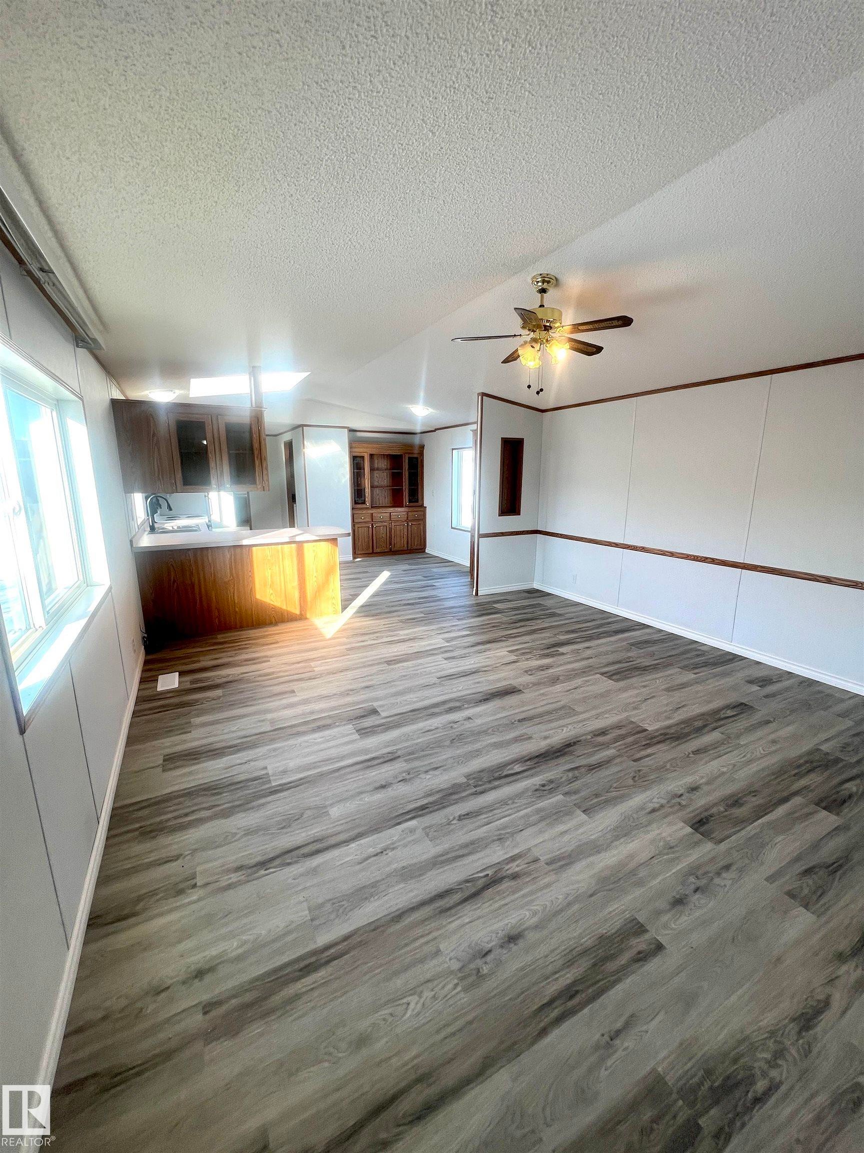 Spacious interior featuring wood-finish flooring, white paneling, and a ceiling fan - 109-4819 51 Ave, Millet, AB - Indoor Photo Showing Other Room