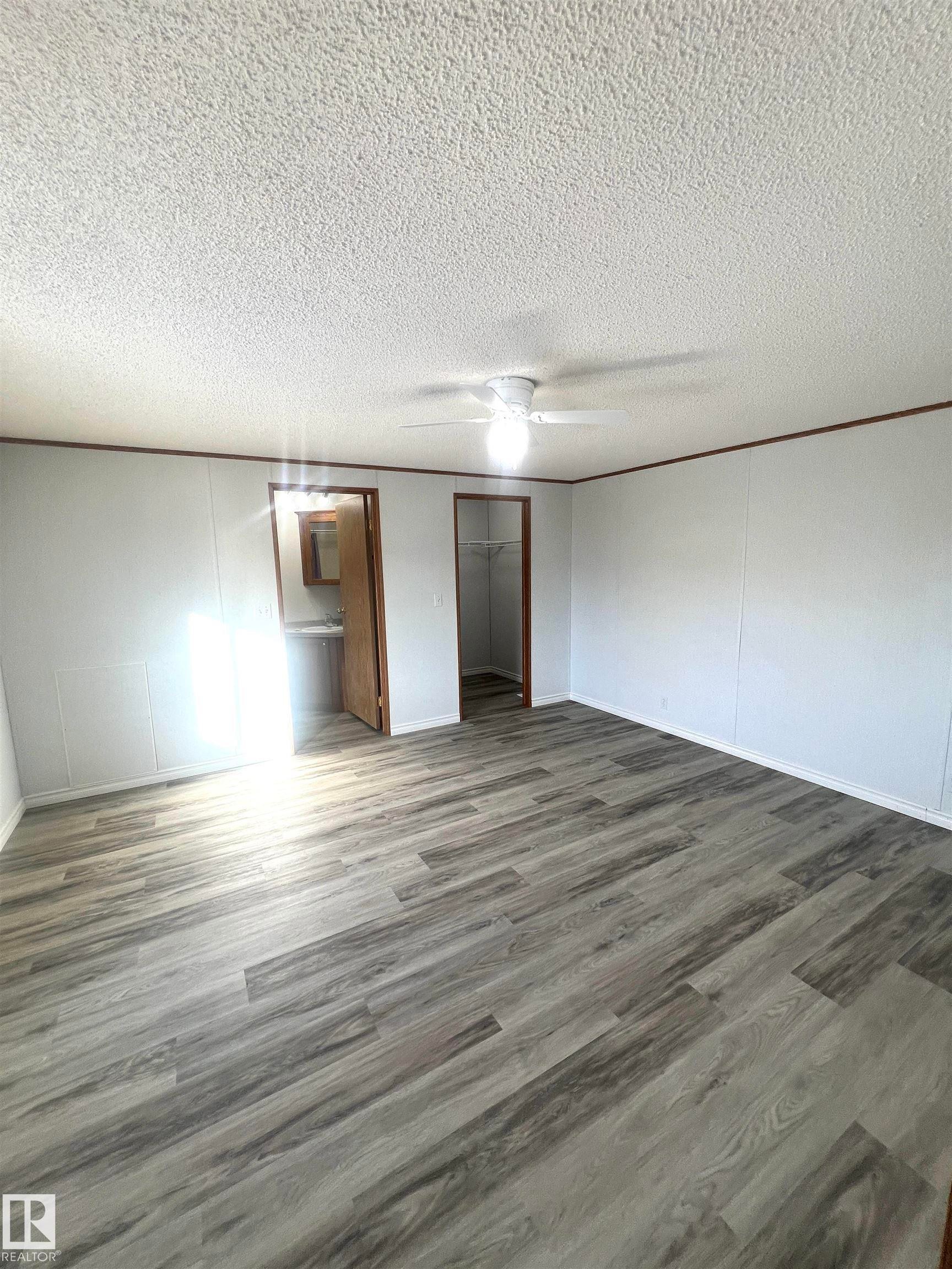 Spacious room featuring wood-finish flooring, white paneled walls, and a ceiling fan - 109-4819 51 Ave, Millet, AB - Indoor Photo Showing Other Room