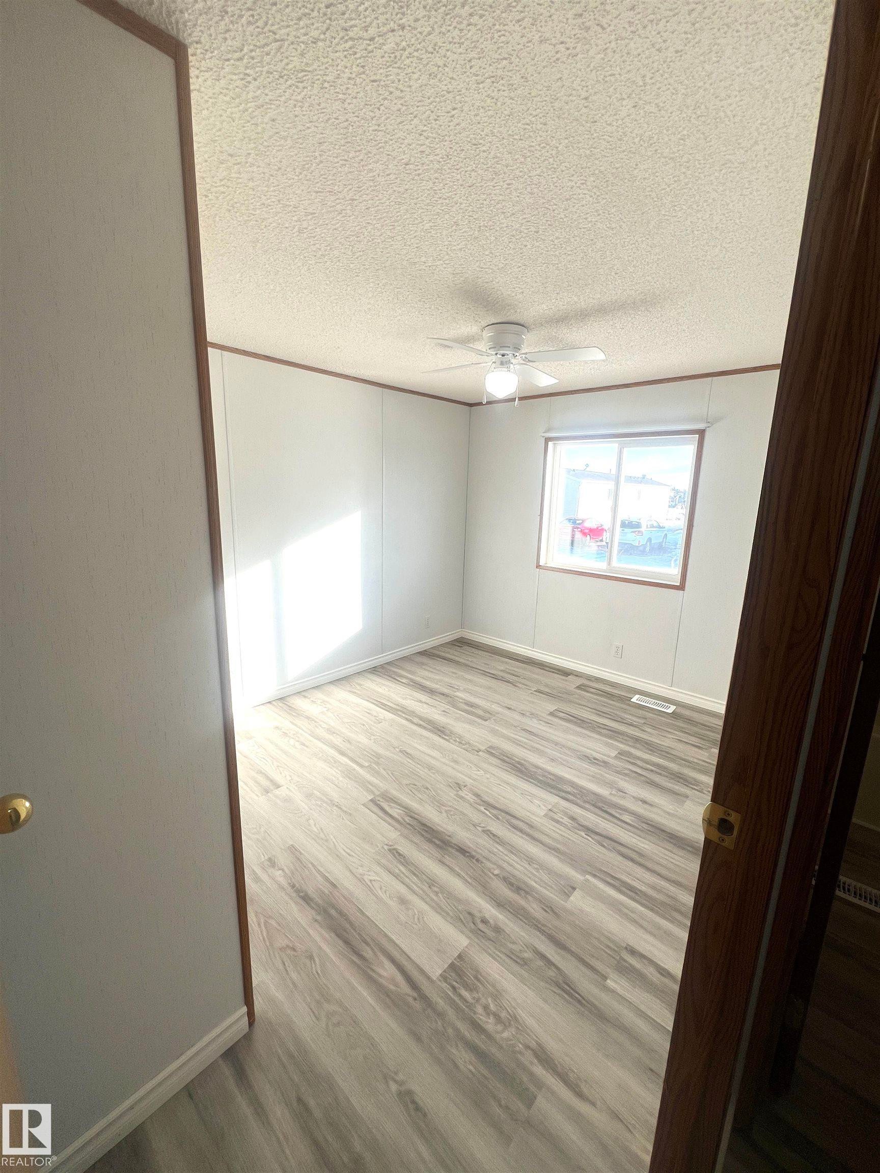 Bright room featuring wood-finish flooring, a ceiling fan with integrated lighting, and a window providing natural illumination - 109-4819 51 Ave, Millet, AB - Indoor Photo Showing Other Room