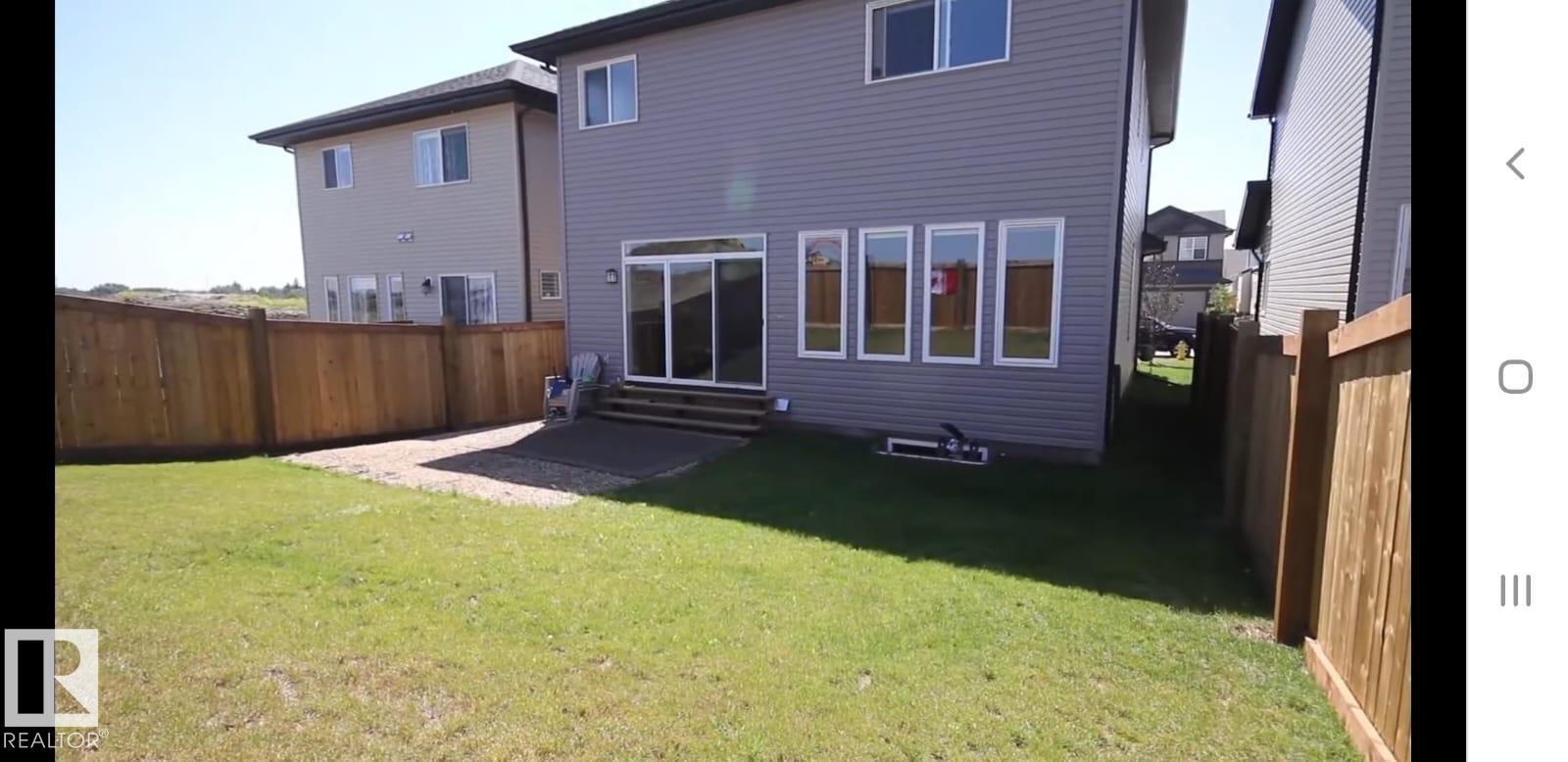 Expansive rear yard featuring a manicured lawn, a wooden privacy fence, a gravel patio area, a sliding glass door, and multiple windows - 9748 205 Street, Edmonton, AB - Outdoor With Exterior