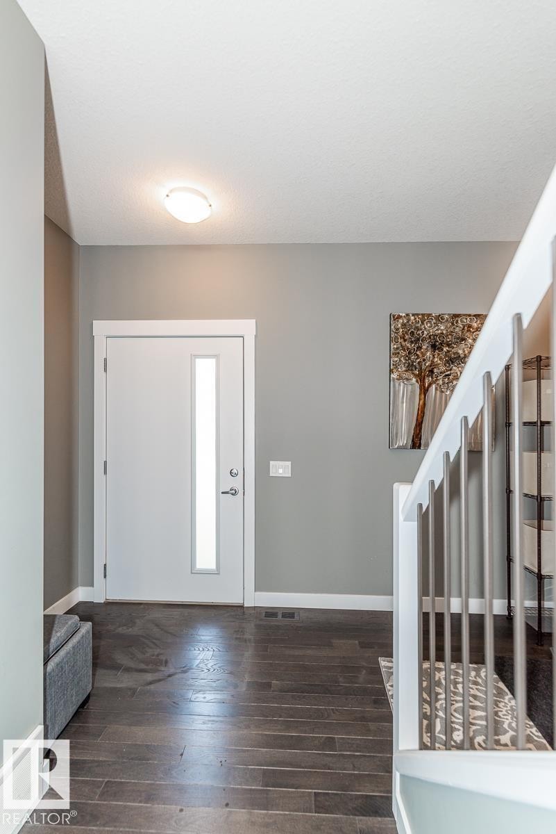 Entry foyer featuring dark wood-finish flooring, a white entry door with vertical frosted glass inlay, and a staircase with white balusters and metal spindles - 9748 205 Street, Edmonton, AB - Indoor Photo Showing Other Room