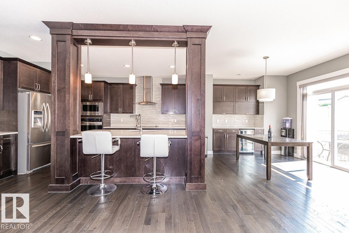 Contemporary kitchen featuring dark wood cabinetry, stainless steel appliances, a breakfast bar with pendant lighting, a tile backsplash, and wood-finish flooring - 9748 205 Street, Edmonton, AB - Indoor Photo Showing Kitchen With Stainless Steel Kitchen With Upgraded Kitchen