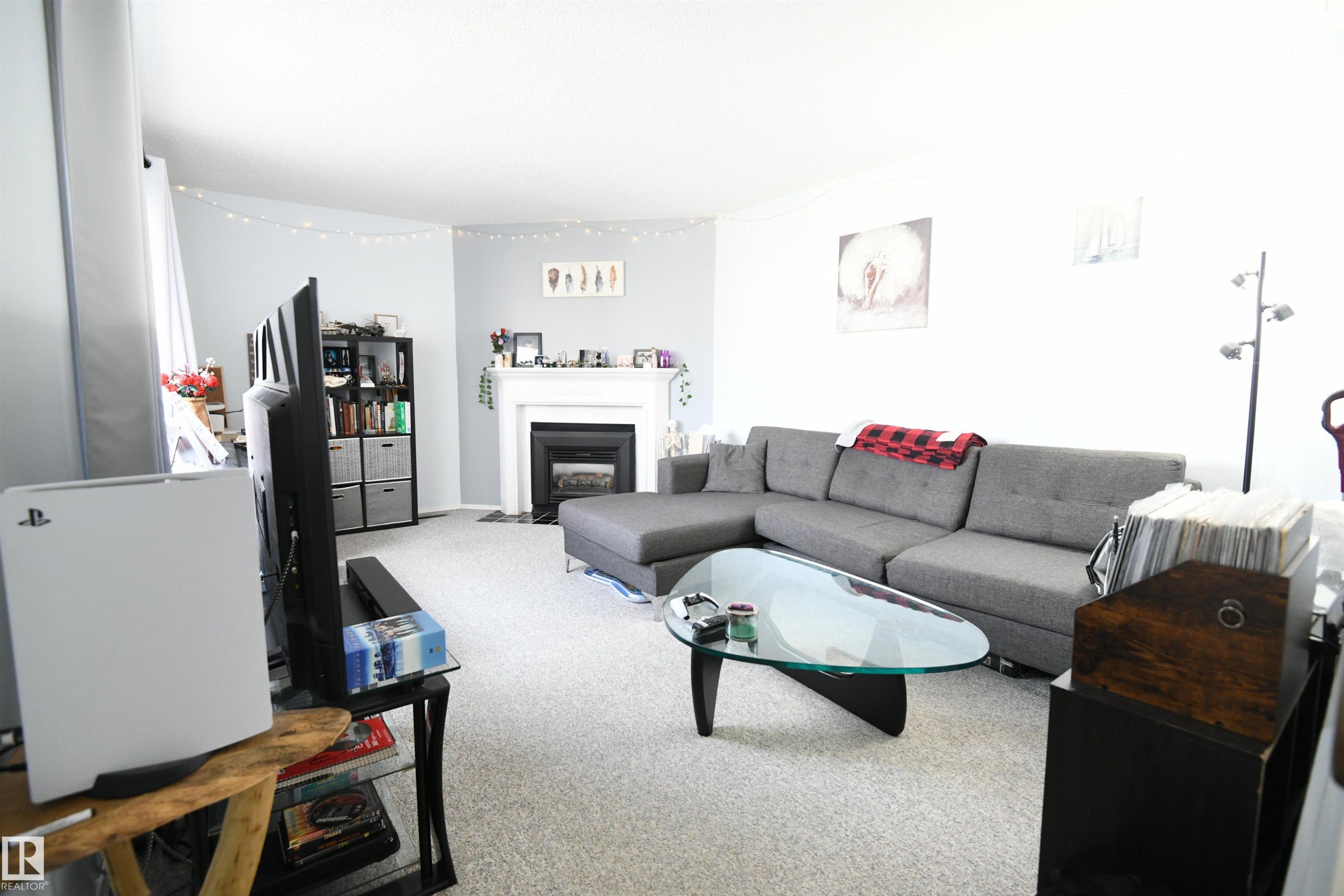 Large windows let in loads of natural light, and the neutral colors in the unit are warm and inviting. The gas corner fireplace makes a great focal point and adds a touch of class and atmosphere, perfect for a quiet, relaxing night in - 5823 Riverbend Road, Edmonton, AB - Indoor Photo Showing Living Room With Fireplace