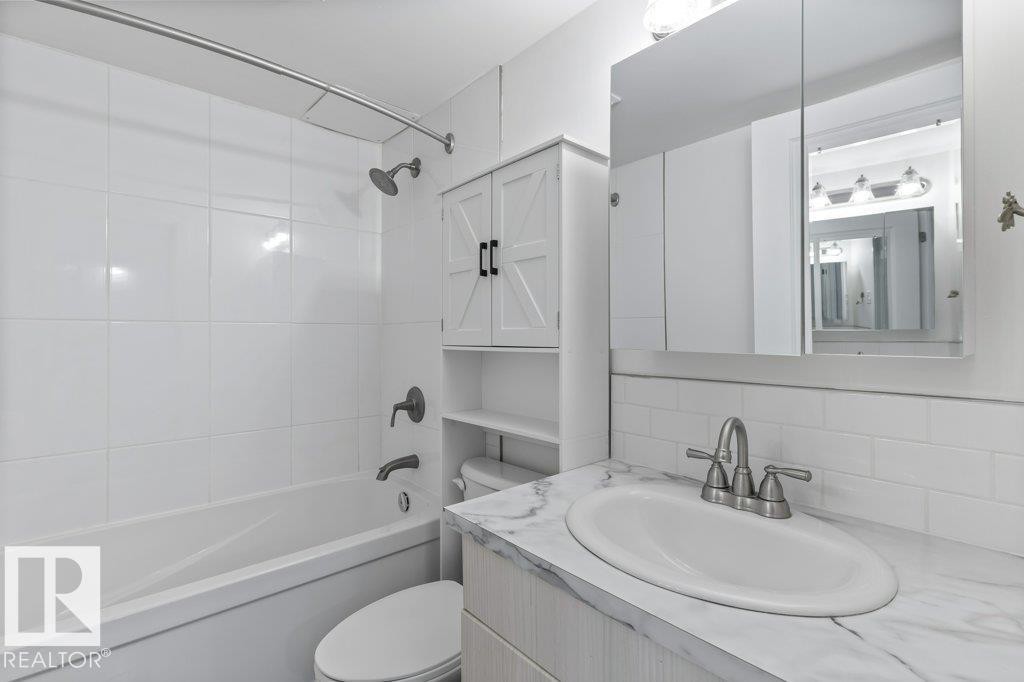 Bathroom featuring a white subway tile backsplash, a vanity with a white countertop, a medicine cabinet, a built-in storage cabinet, and a soaker tub. - 101 8604 Gateway Boulevard, Edmonton, AB - Indoor Photo Showing Bathroom