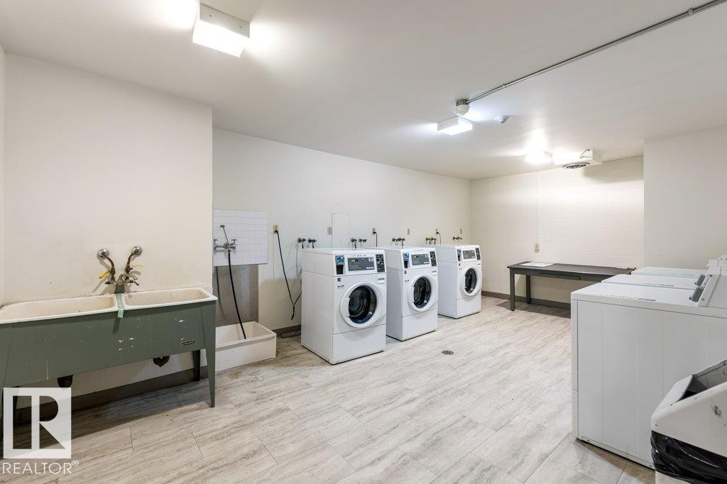 Dedicated laundry facility featuring multiple washing machines, dryers & a utility sink. - 101 8604 Gateway Boulevard, Edmonton, AB - Indoor Photo Showing Laundry Room