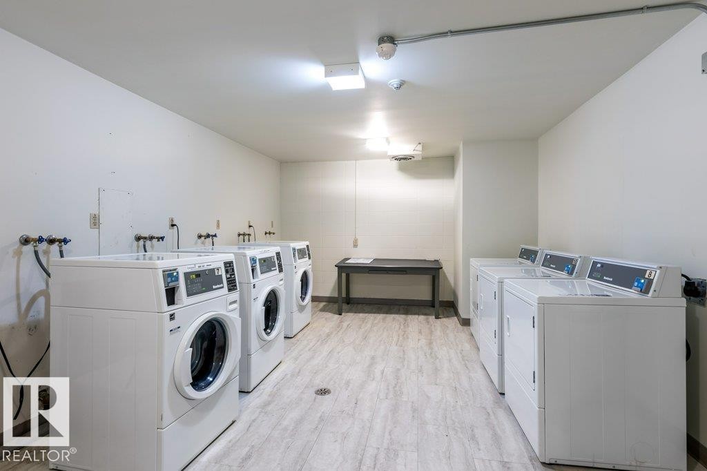 Dedicated laundry facility featuring multiple washing machines, dryers & a utility sink. - 101 8604 Gateway Boulevard, Edmonton, AB - Indoor Photo Showing Laundry Room