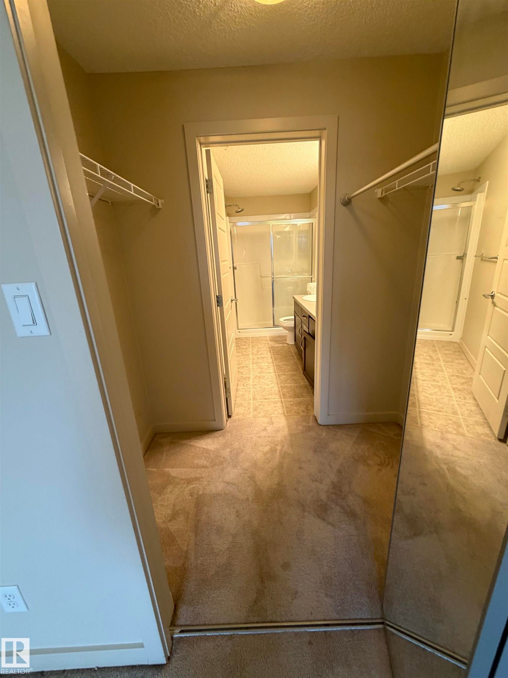 Walk-in closet with carpet flooring, shelving, and a mirrored wall - 313 6084 Stanton Drive, Edmonton, AB - Indoor Photo Showing Other Room