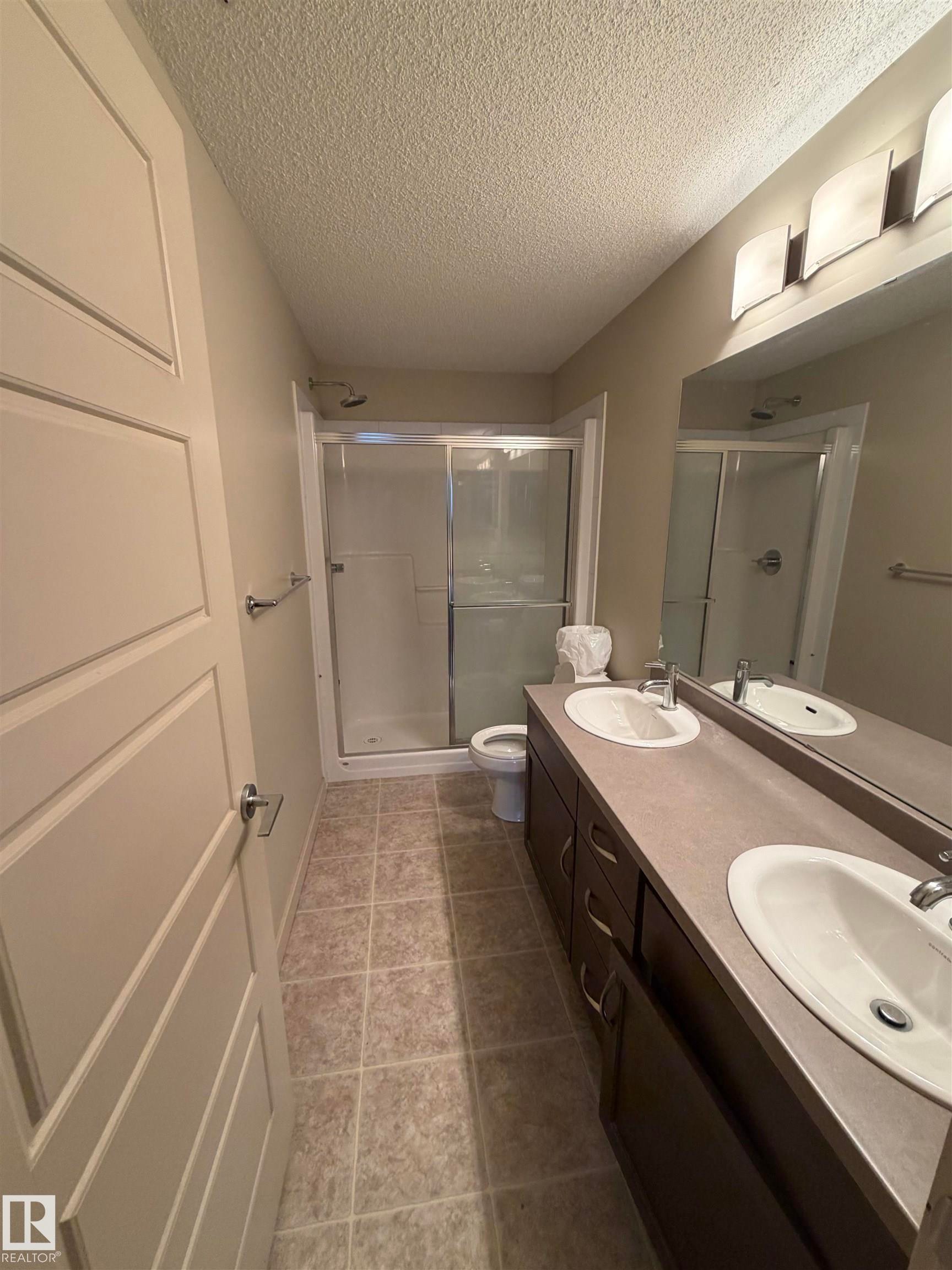 Well-appointed bathroom featuring a double vanity with two sinks, a large mirror, and an enclosed shower - 313 6084 Stanton Drive, Edmonton, AB - Indoor Photo Showing Bathroom