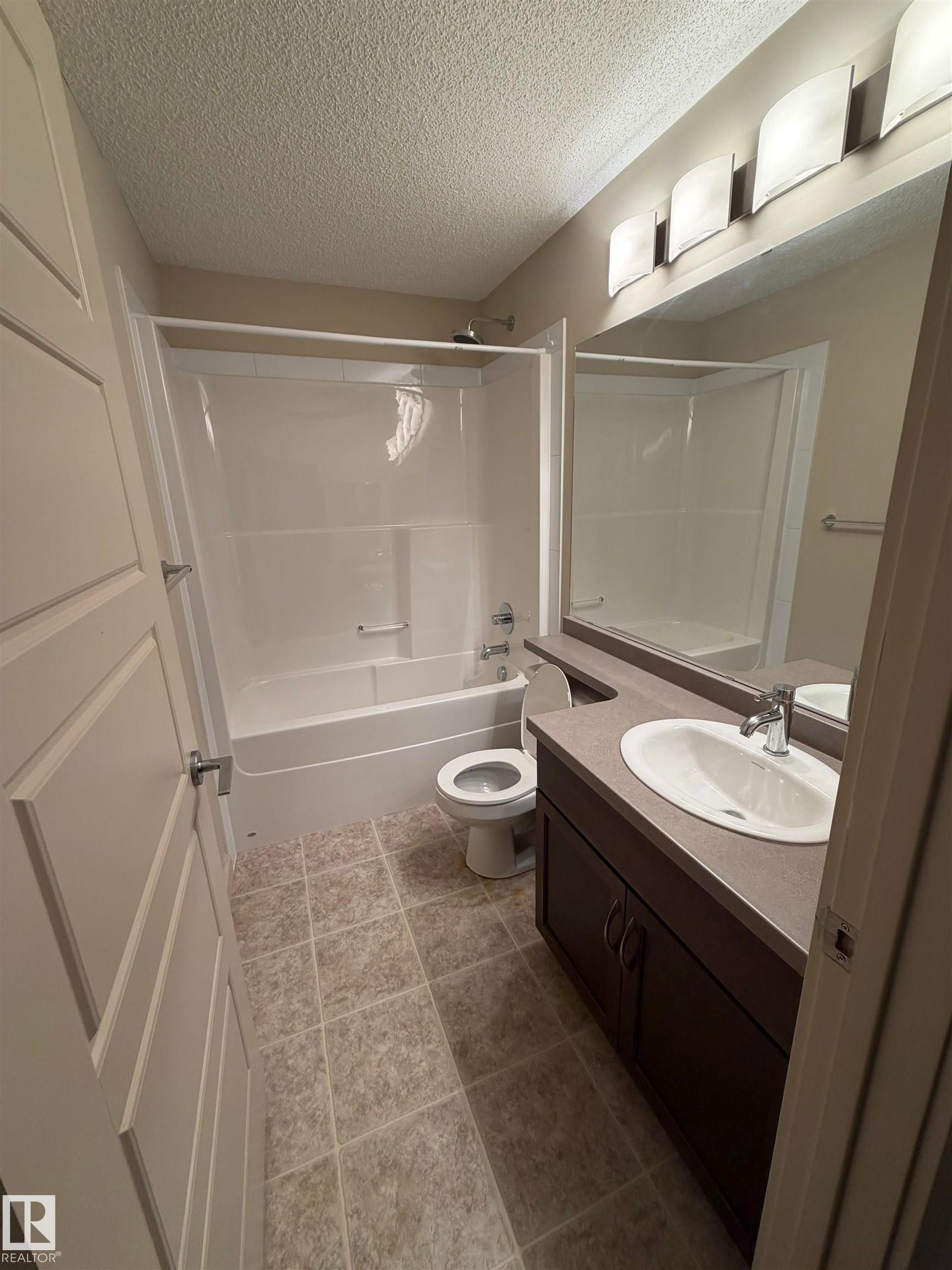 Well-maintained bathroom featuring a vanity with an integrated sink and countertop, a toilet, and a combination bathtub and shower with a white surround - 313 6084 Stanton Drive, Edmonton, AB - Indoor Photo Showing Bathroom