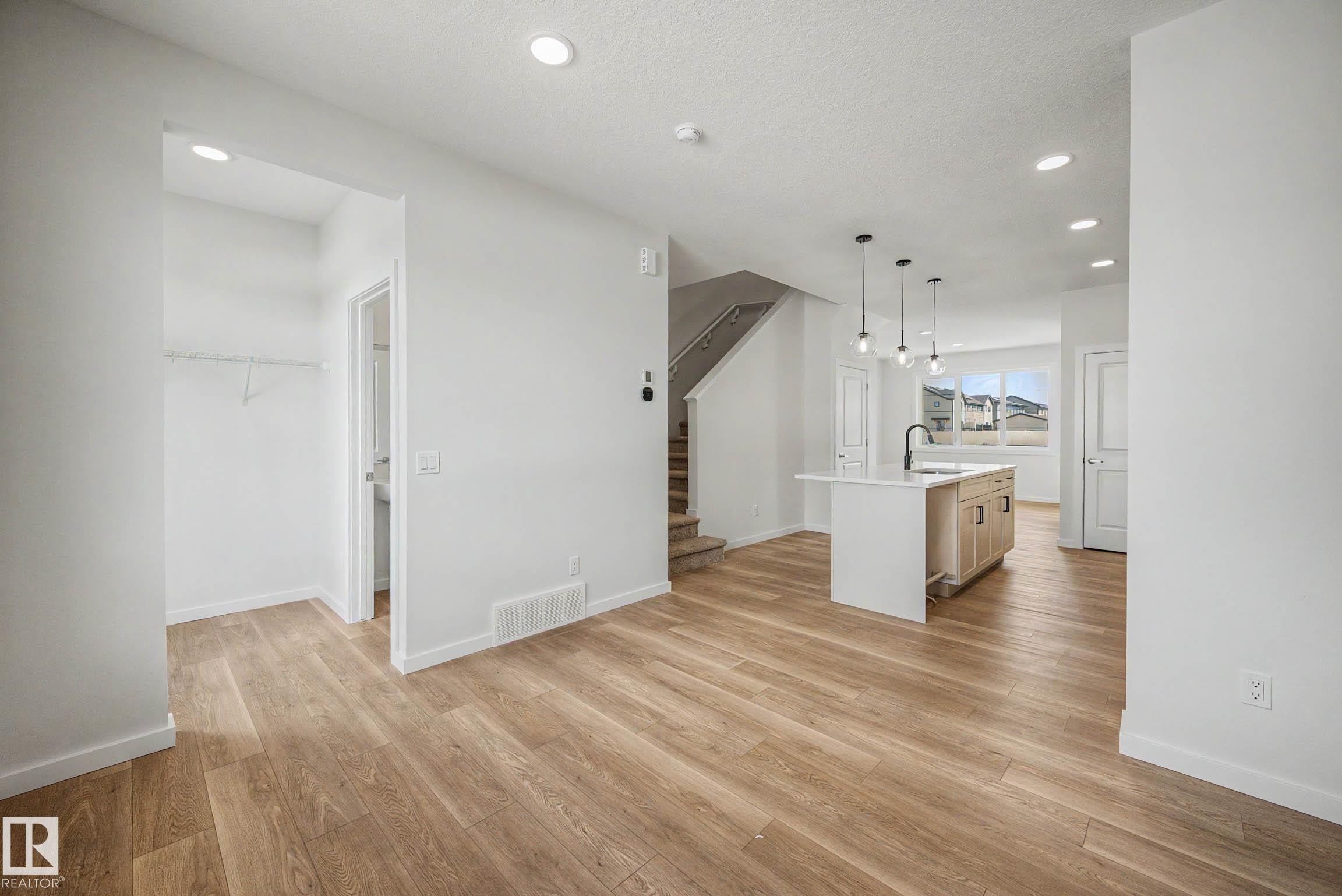 Open-concept living space featuring wood-finish flooring, recessed lighting, and a kitchen island with a built-in sink and pendant lighting - 720 Southfork Drive, Leduc, AB - Indoor