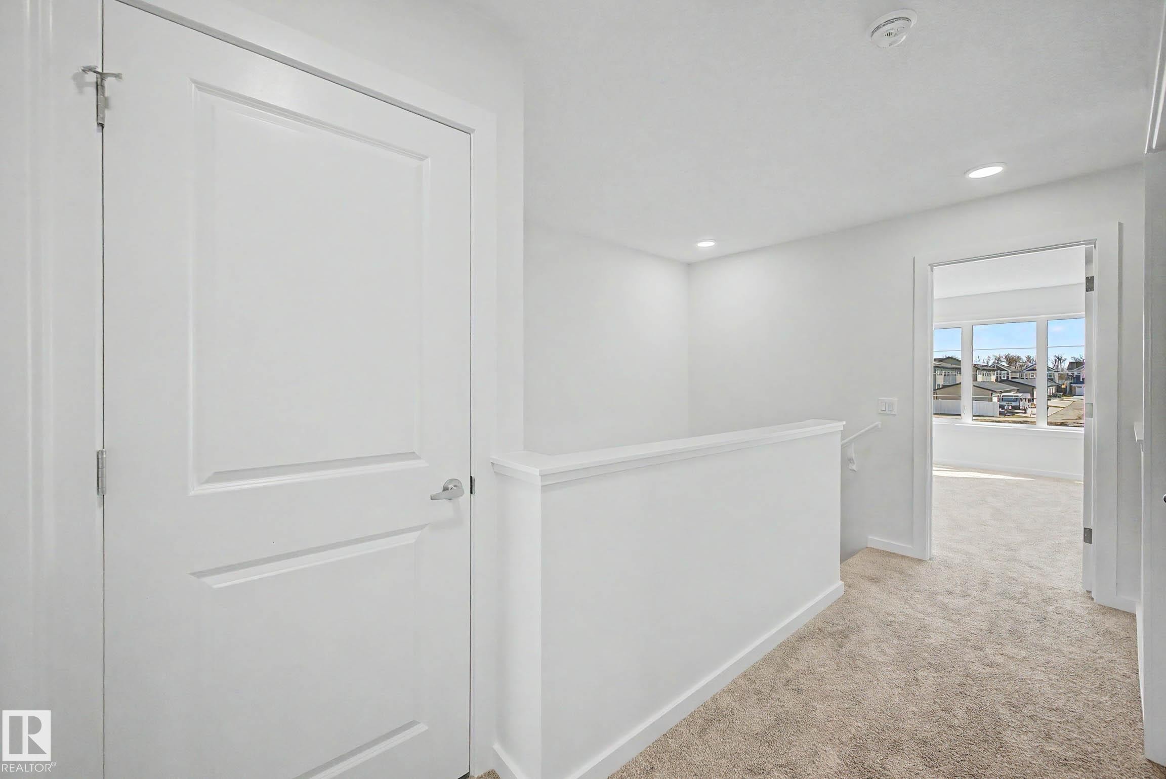 Carpeted hallway featuring a white paneled door with chrome hardware, white painted walls, recessed lighting, and a white half-wall railing - 720 Southfork Drive, Leduc, AB - Indoor Photo Showing Other Room