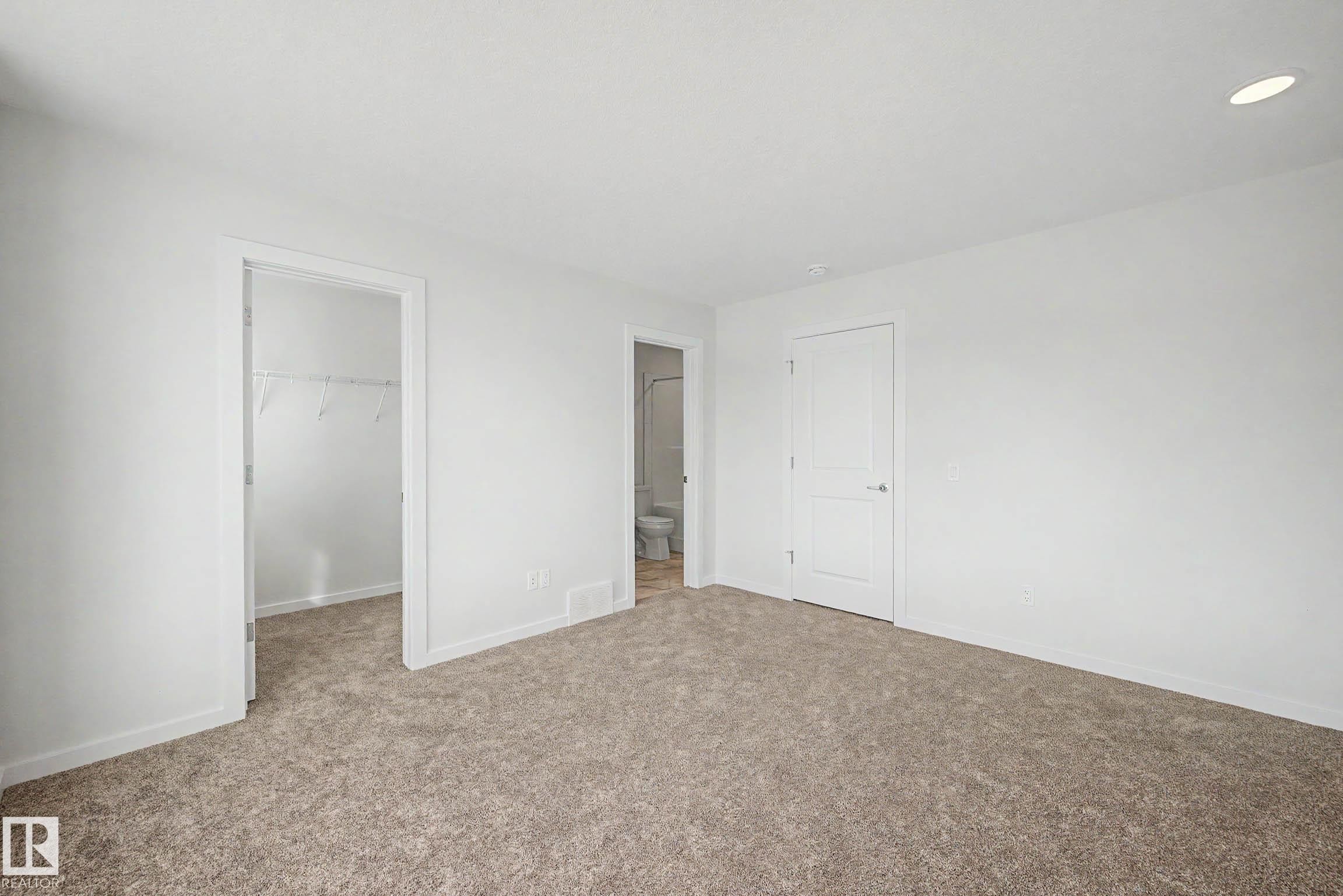 Carpeted room featuring white walls, a white interior door with a silver handle, and an open doorway revealing a closet with wire shelving - 720 Southfork Drive, Leduc, AB - Indoor Photo Showing Other Room