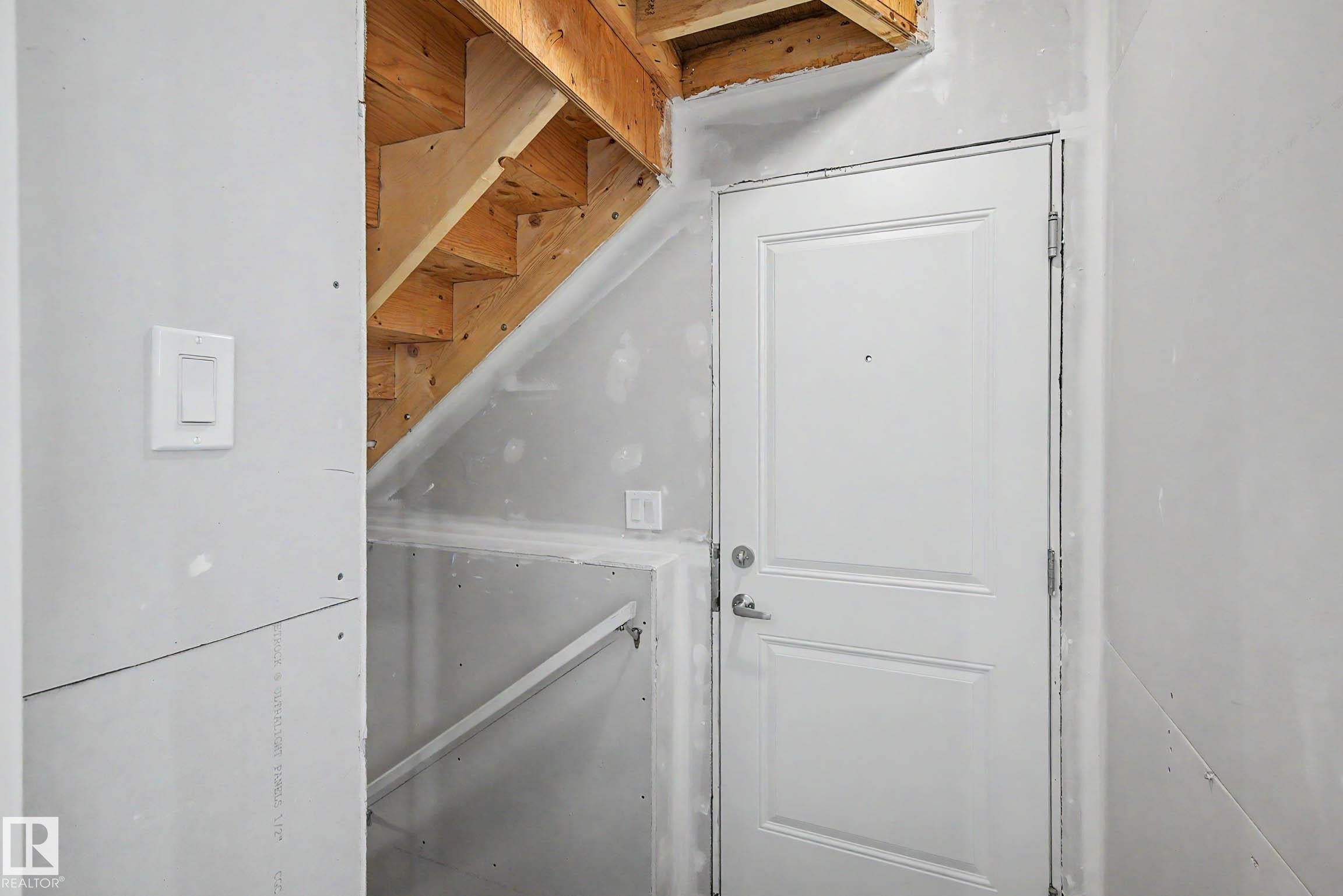 Unfinished interior space featuring exposed wood staircase framing, drywall installation, and a paneled white door with a lever handle - 720 Southfork Drive, Leduc, AB - Indoor Photo Showing Other Room