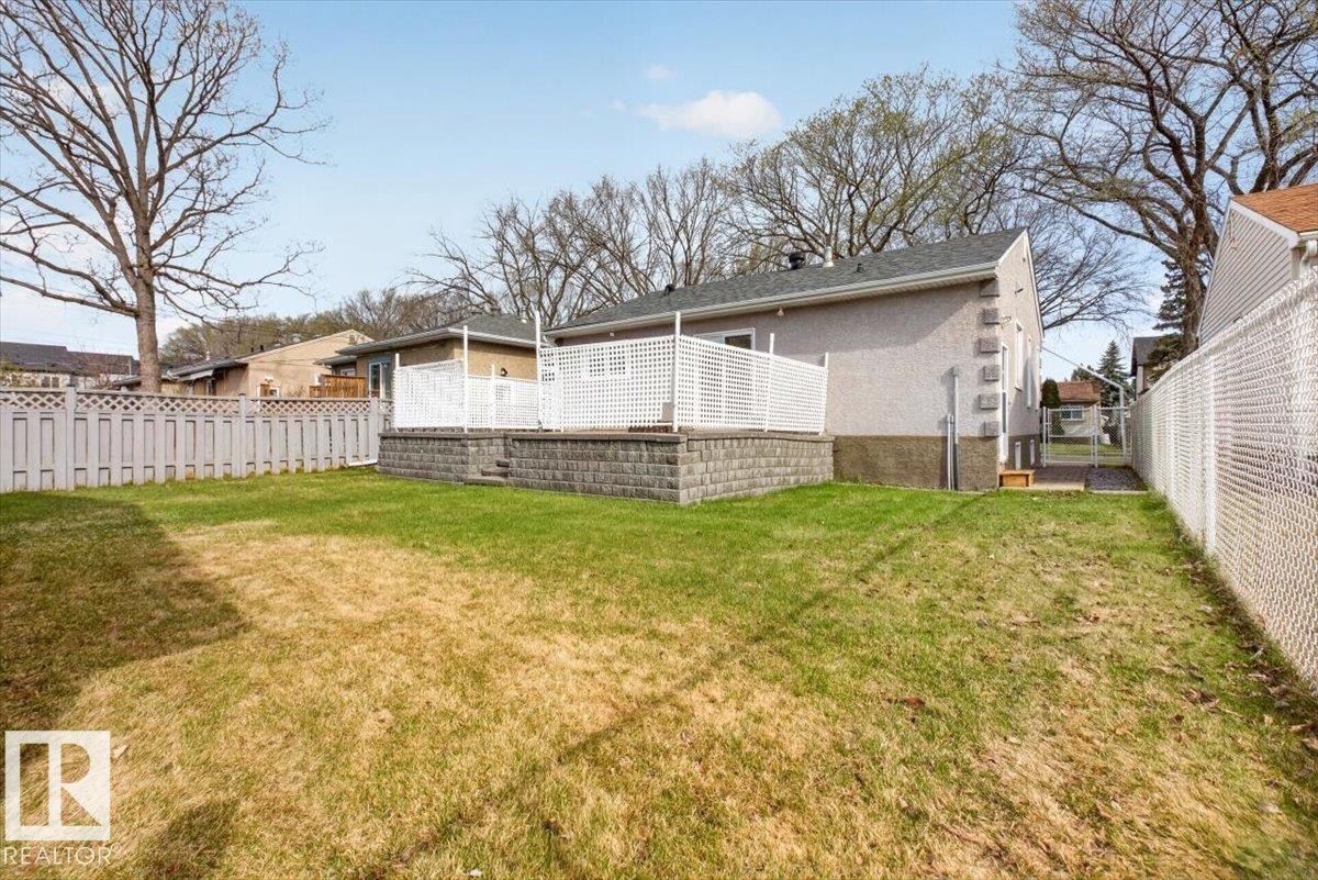 Expansive grassy yard with a raised patio featuring white lattice railing - 9723 65 Avenue, Edmonton, AB - Outdoor