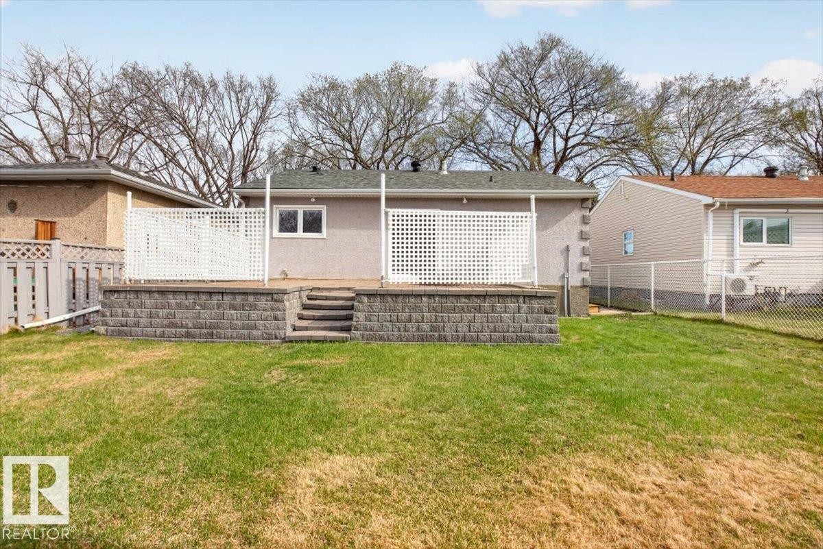 Expansive backyard featuring a tiered retaining wall, a raised concrete patio, and white lattice privacy screens - 9723 65 Avenue, Edmonton, AB - Outdoor