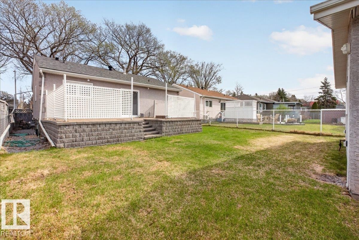 Rear exterior featuring an elevated deck with white lattice privacy screening, concrete block retaining wall, and backyard access via steps - 9723 65 Avenue, Edmonton, AB - Outdoor