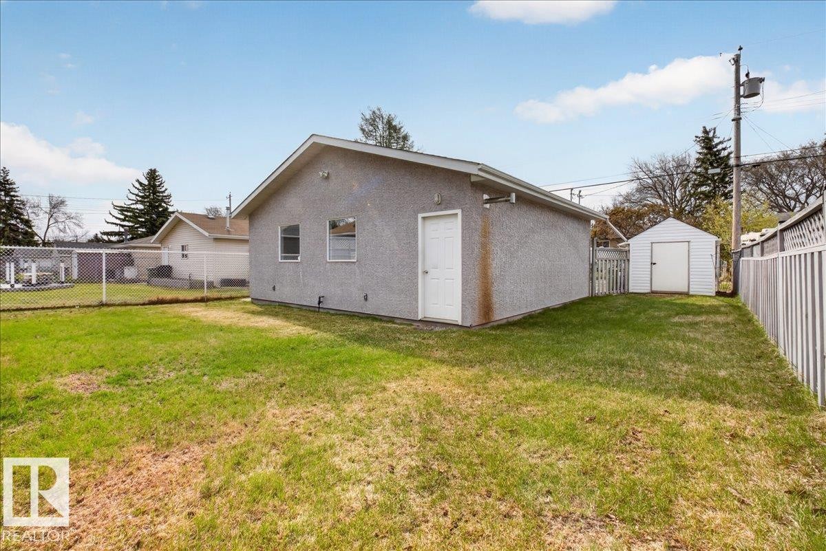 Detached garage featuring a stucco exterior, a white entry door, two windows, and an adjacent storage shed - 9723 65 Avenue, Edmonton, AB - Outdoor
