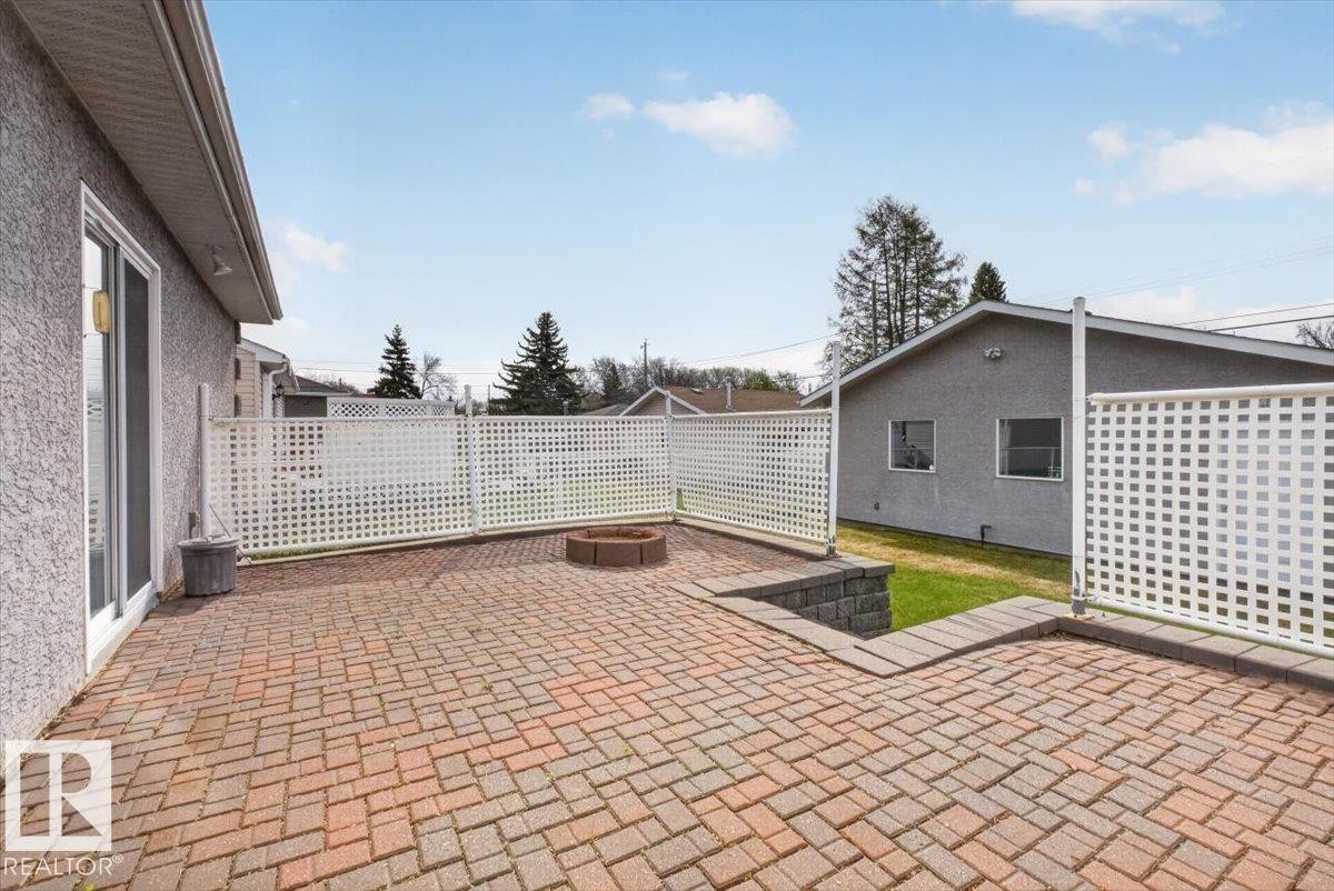 Brick paver patio featuring a built-in fire pit, privacy lattice fencing, and a retaining wall with stone block accents - 9723 65 Avenue, Edmonton, AB - Outdoor With Deck Patio Veranda With Exterior