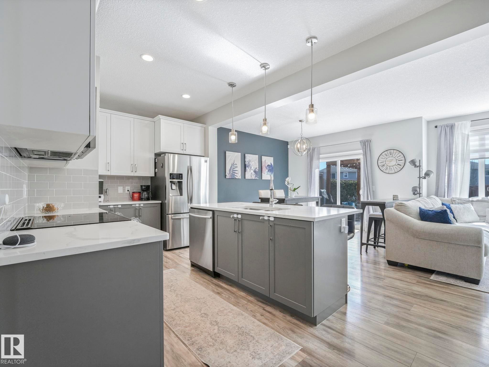 Modern kitchen featuring white and gray cabinetry, stainless steel appliances, white countertops, a subway tile backsplash, and an island with pendant lighting - 3817 Robins Crescent, Edmonton, AB - Indoor Photo Showing Kitchen With Stainless Steel Kitchen With Upgraded Kitchen
