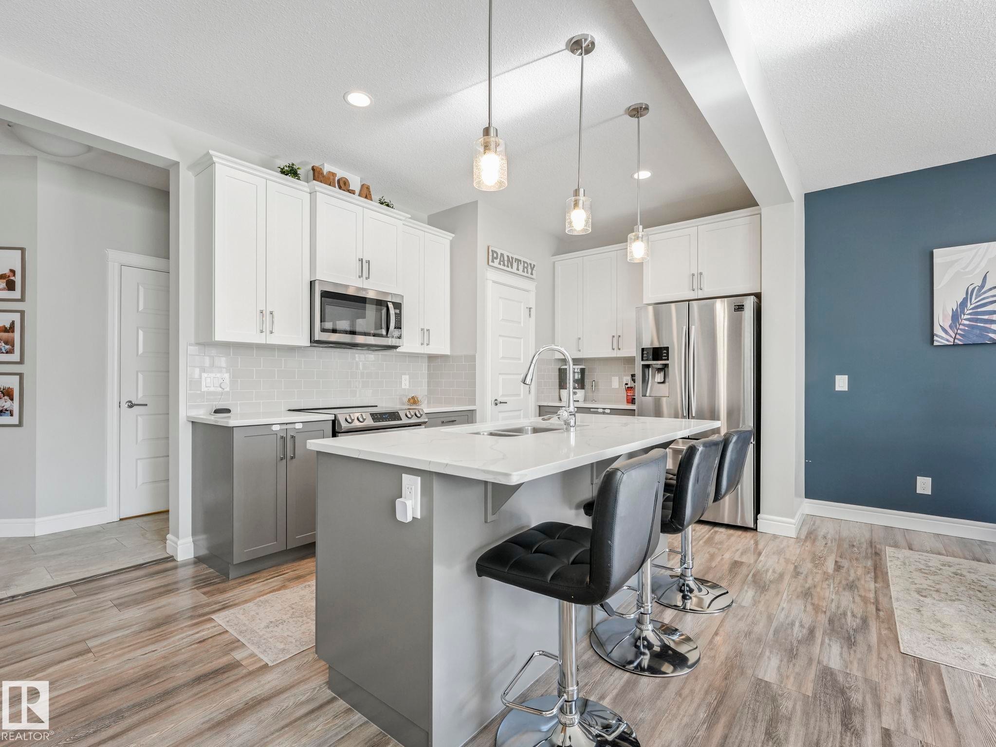 Modern kitchen featuring a central island with countertop seating, stainless steel appliances, two-tone cabinetry, wood-finish flooring, and subway tile backsplash - 3817 Robins Crescent, Edmonton, AB - Indoor Photo Showing Kitchen With Stainless Steel Kitchen With Upgraded Kitchen