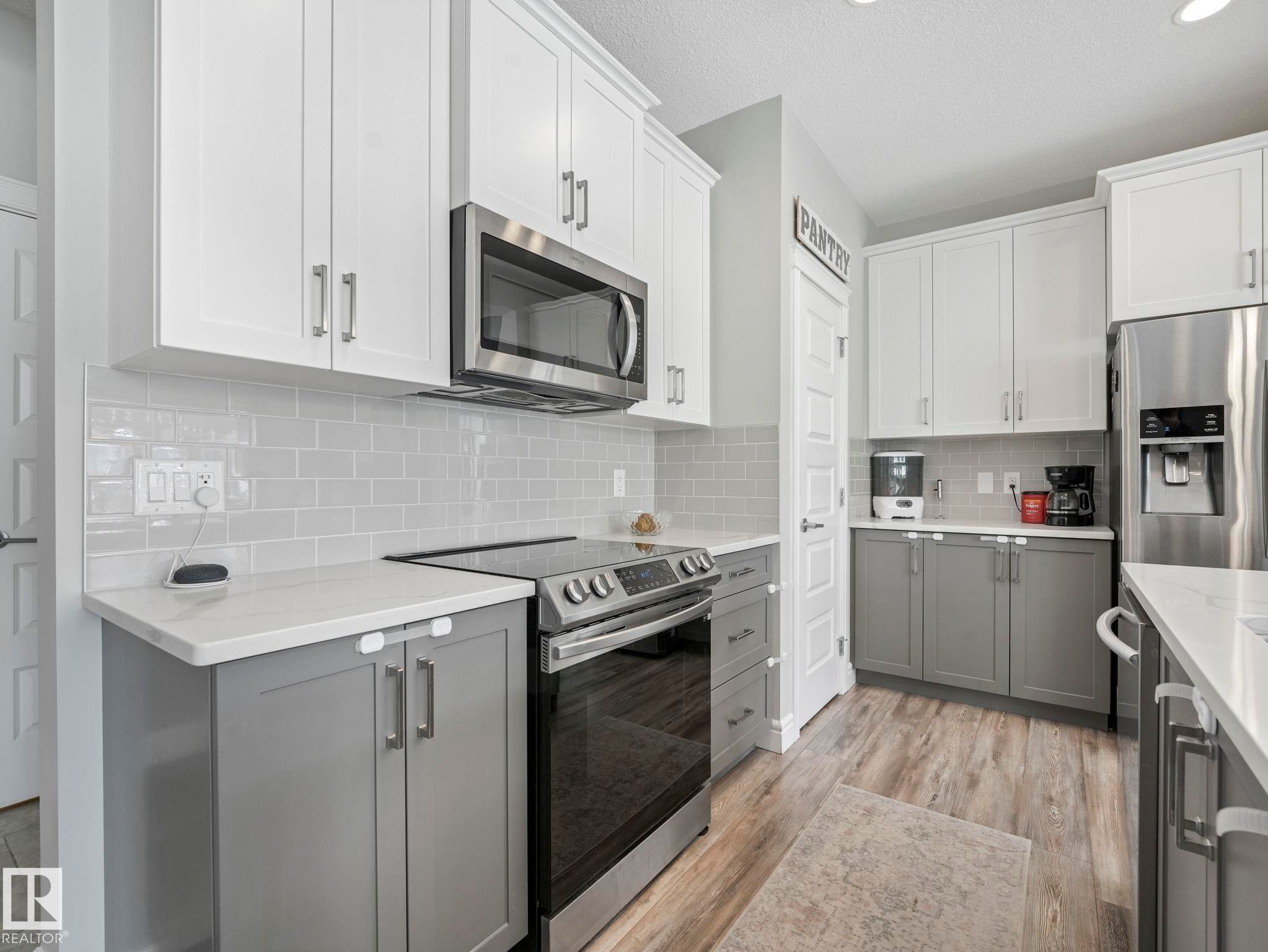 Modern kitchen featuring two-tone cabinetry, stainless steel appliances, light subway tile backsplash, and wood-finish flooring - 3817 Robins Crescent, Edmonton, AB - Indoor Photo Showing Kitchen With Stainless Steel Kitchen With Upgraded Kitchen