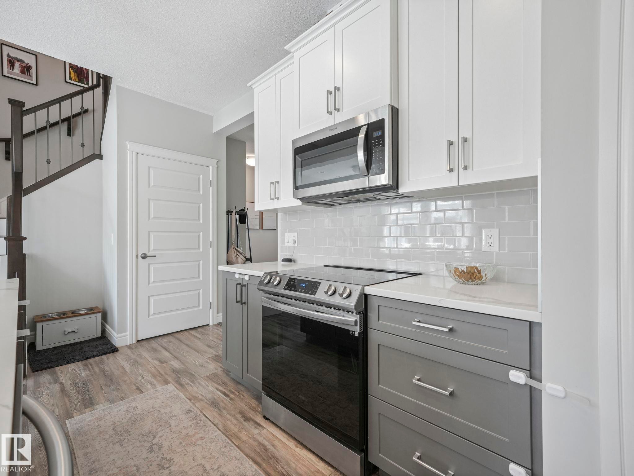 Modern kitchen featuring two-tone cabinetry with white upper cabinets and gray lower cabinets, complemented by stainless steel appliances - 3817 Robins Crescent, Edmonton, AB - Indoor Photo Showing Kitchen With Upgraded Kitchen