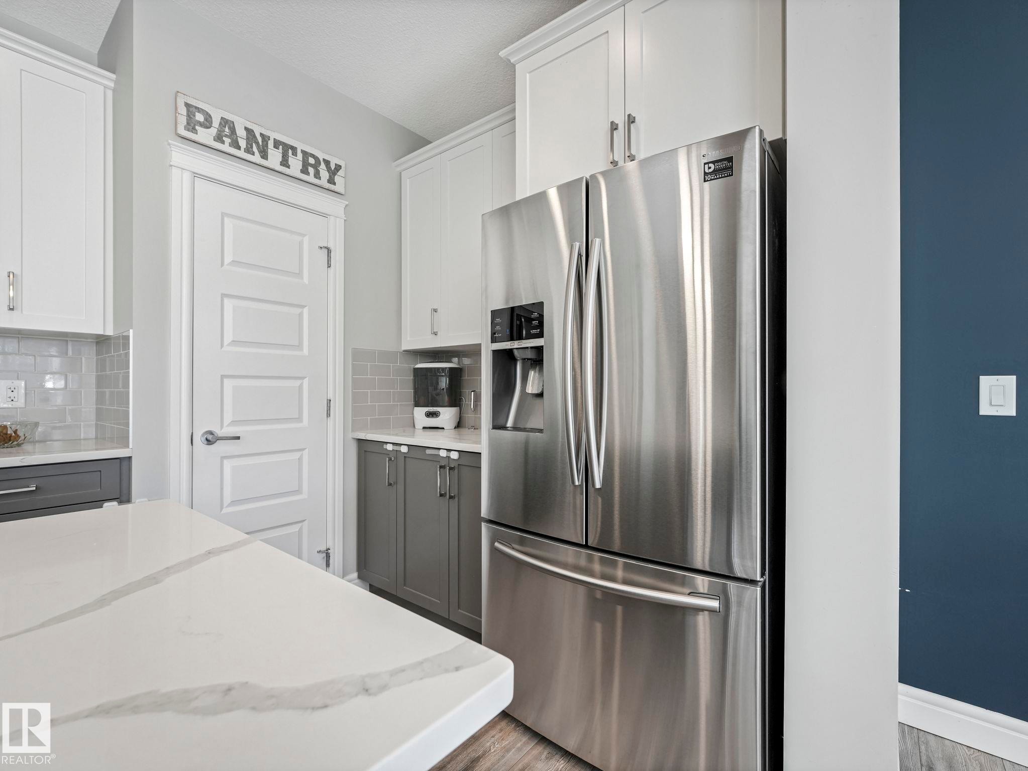 Kitchen featuring a large stainless steel refrigerator, white and gray cabinetry, light gray subway tile backsplash, and a white countertop with subtle veining - 3817 Robins Crescent, Edmonton, AB - Indoor Photo Showing Kitchen With Stainless Steel Kitchen