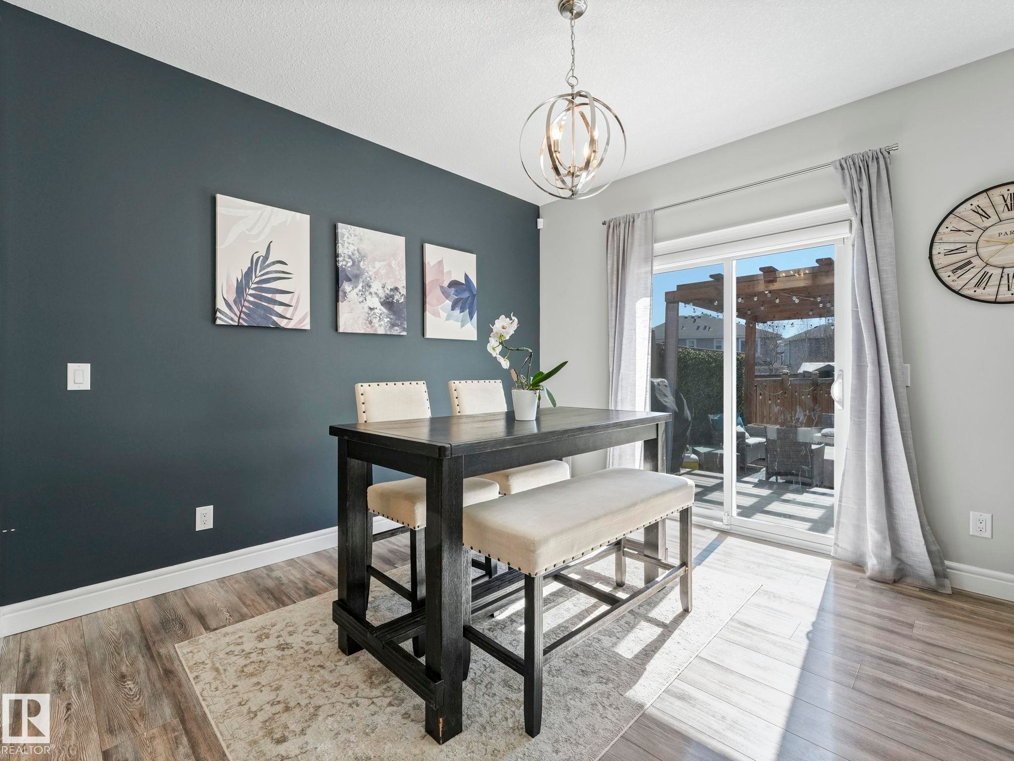 Dining area featuring wood-finish flooring, a contemporary overhead light fixture, and a sliding glass door leading to a patio with a pergola - 3817 Robins Crescent, Edmonton, AB - Indoor Photo Showing Dining Room