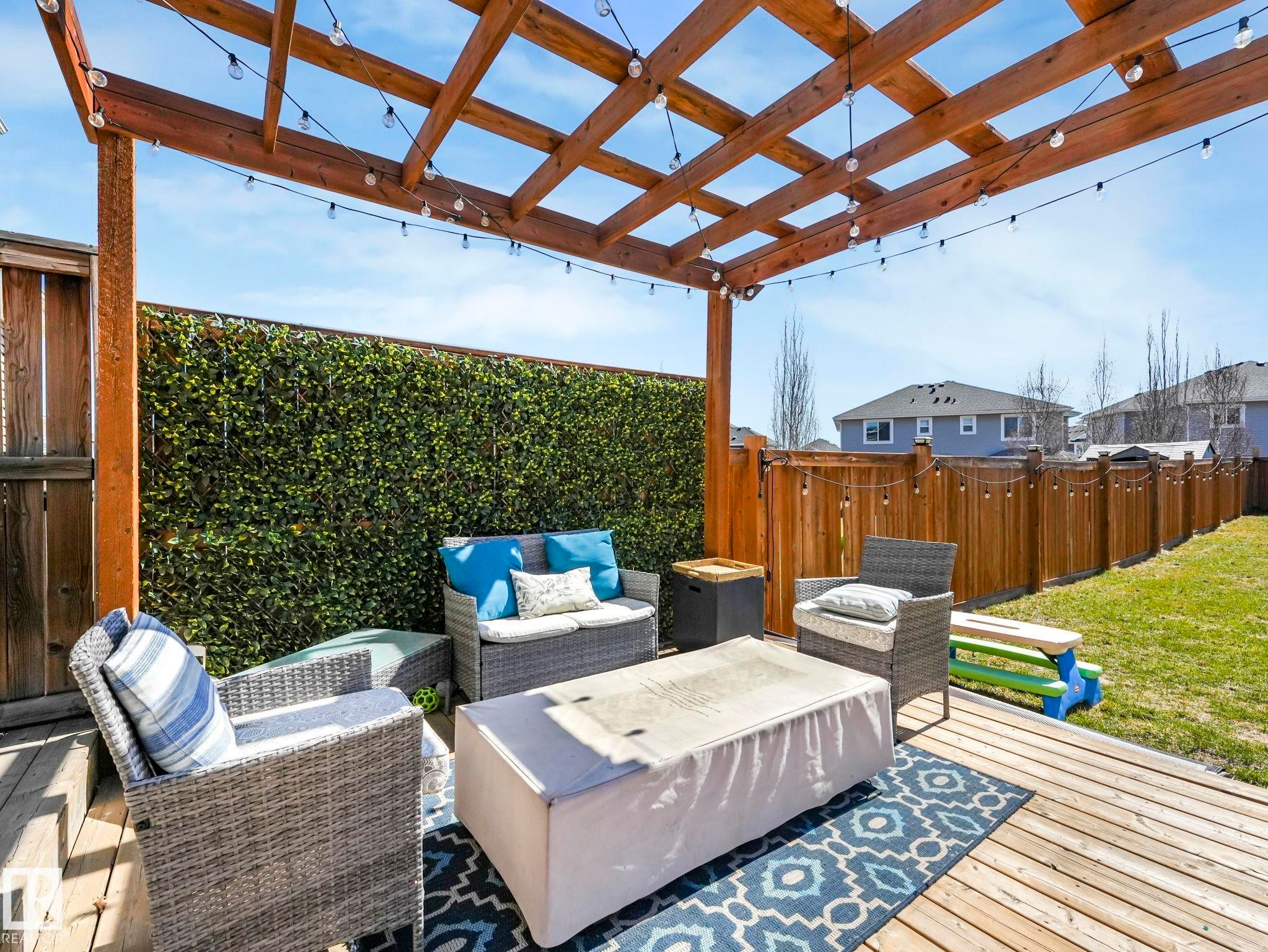 Expansive wood deck with an overhead pergola, artificial green privacy wall, string lighting, and a fenced perimeter - 3817 Robins Crescent, Edmonton, AB - Outdoor With Deck Patio Veranda With Exterior