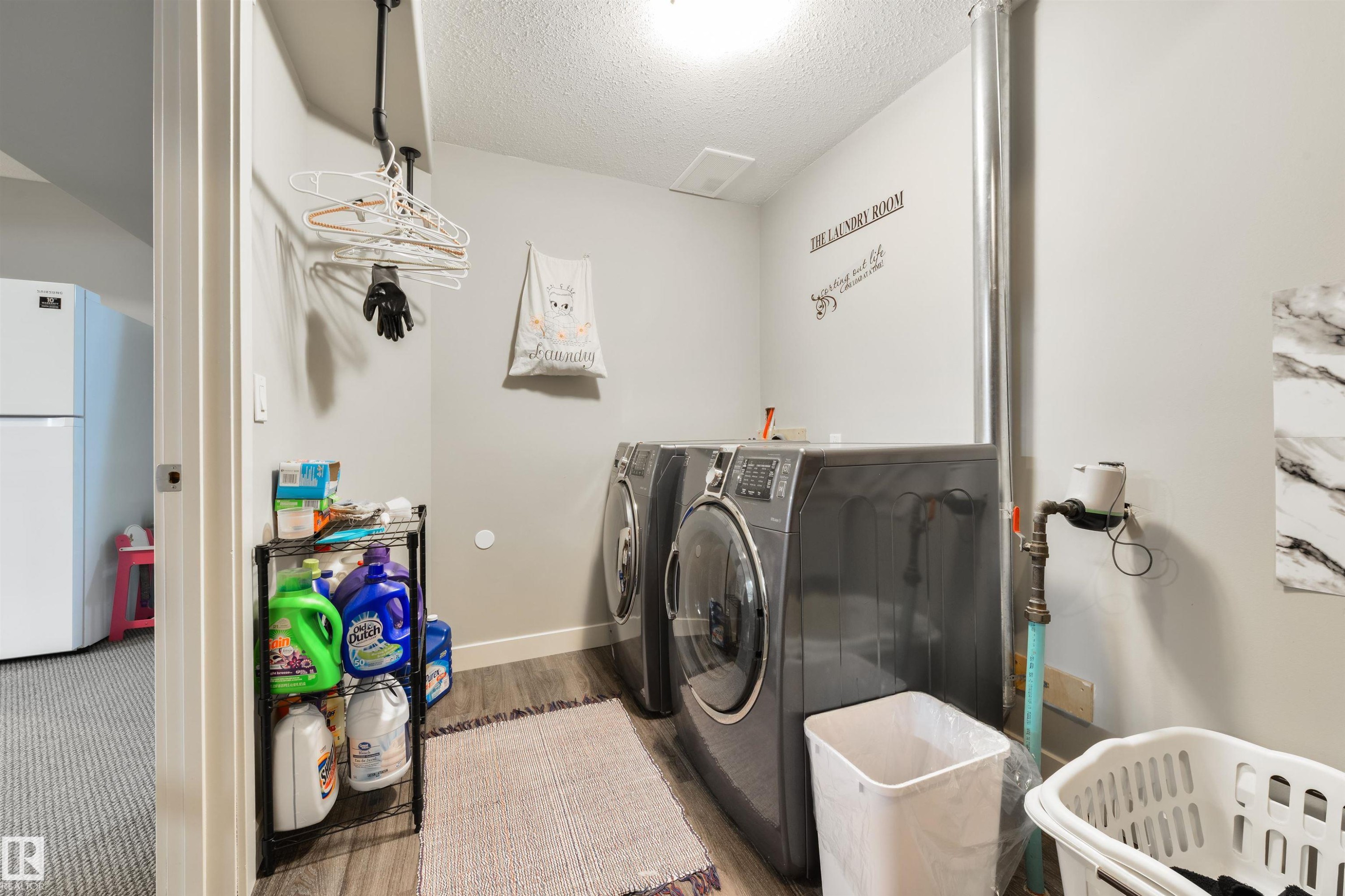 Dedicated laundry area featuring a front-loading washer and dryer set, wood-finish flooring, and light gray walls - 4914 47 Street, Redwater, AB - Indoor Photo Showing Laundry Room