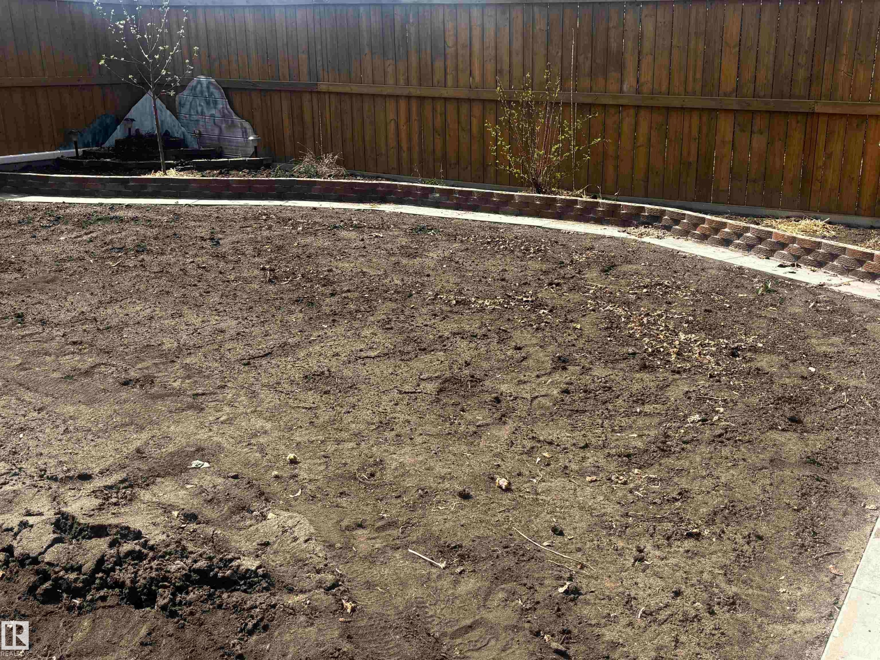Expansive outdoor space featuring a wood fence perimeter, a curved brick-edged garden bed, a concrete border, and prepared soil for landscaping - 4914 47 Street, Redwater, AB - Outdoor