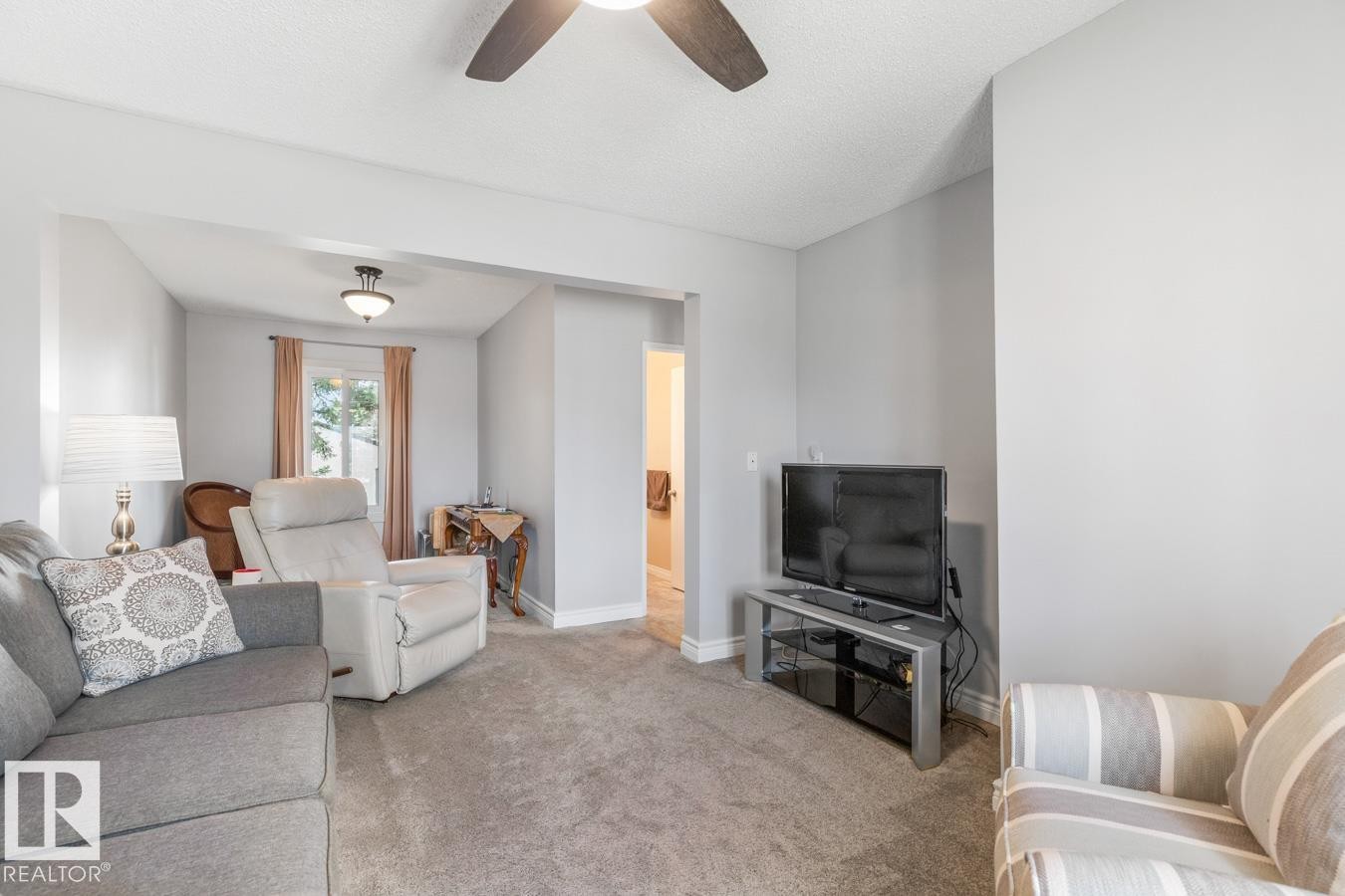 Carpeted living area featuring light gray walls, a ceiling fan with integrated lighting, and a window with natural light - 10502 158 Street, Edmonton, AB - Indoor Photo Showing Living Room