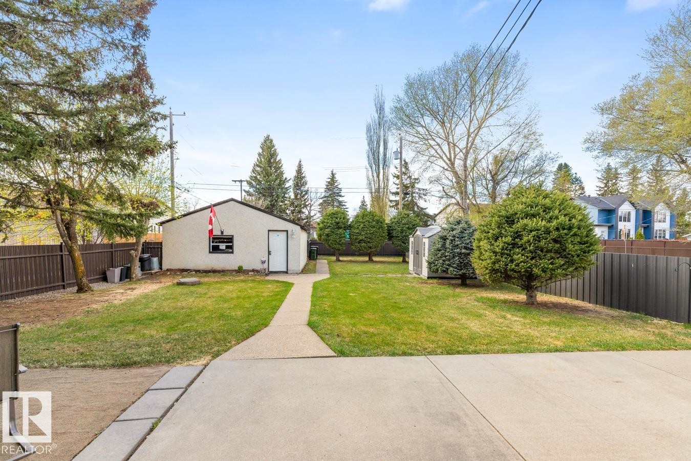 Expansive backyard featuring a detached structure with a white entry door, a separate storage shed, mature trees, and a concrete pathway leading to the structure - 10502 158 Street, Edmonton, AB - Outdoor