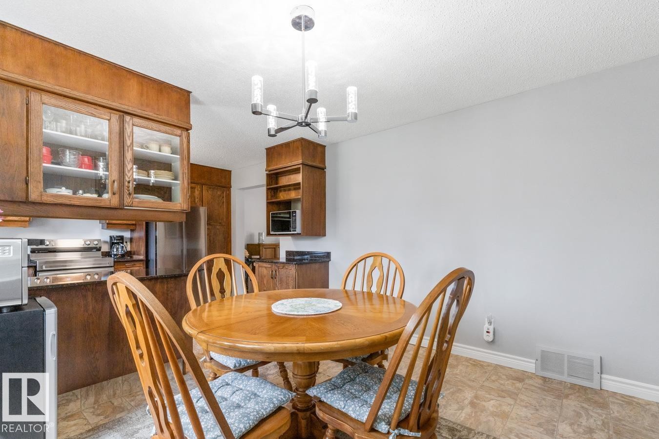Dining area featuring a light wood-finish round table, a contemporary chandelier, light gray painted walls, and light-toned floor tiling - 10502 158 Street, Edmonton, AB - Indoor Photo Showing Dining Room