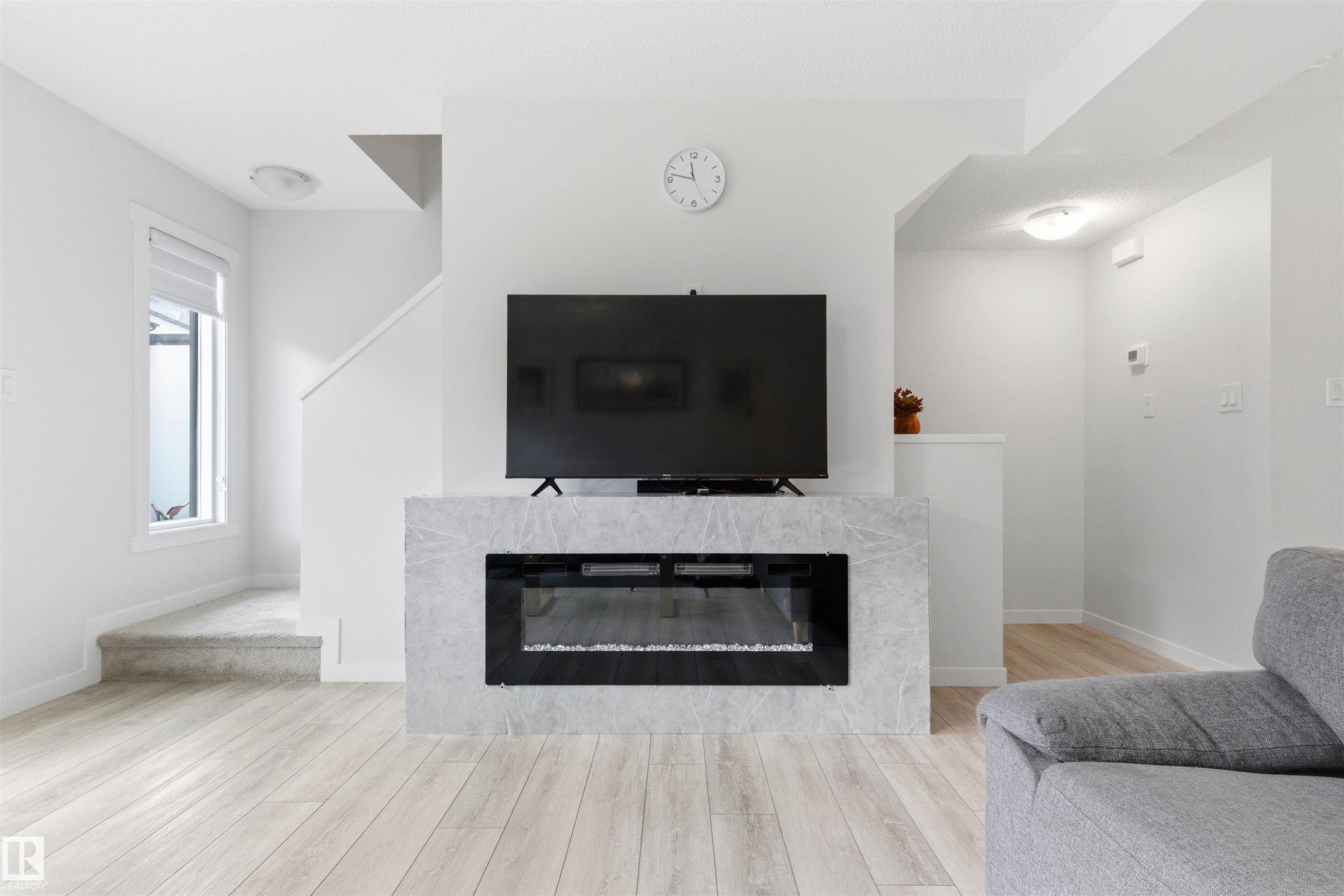 Contemporary electric fireplace with a light-toned stone surround - 9 850 Secord Boulevard, Edmonton, AB - Indoor Photo Showing Living Room With Fireplace