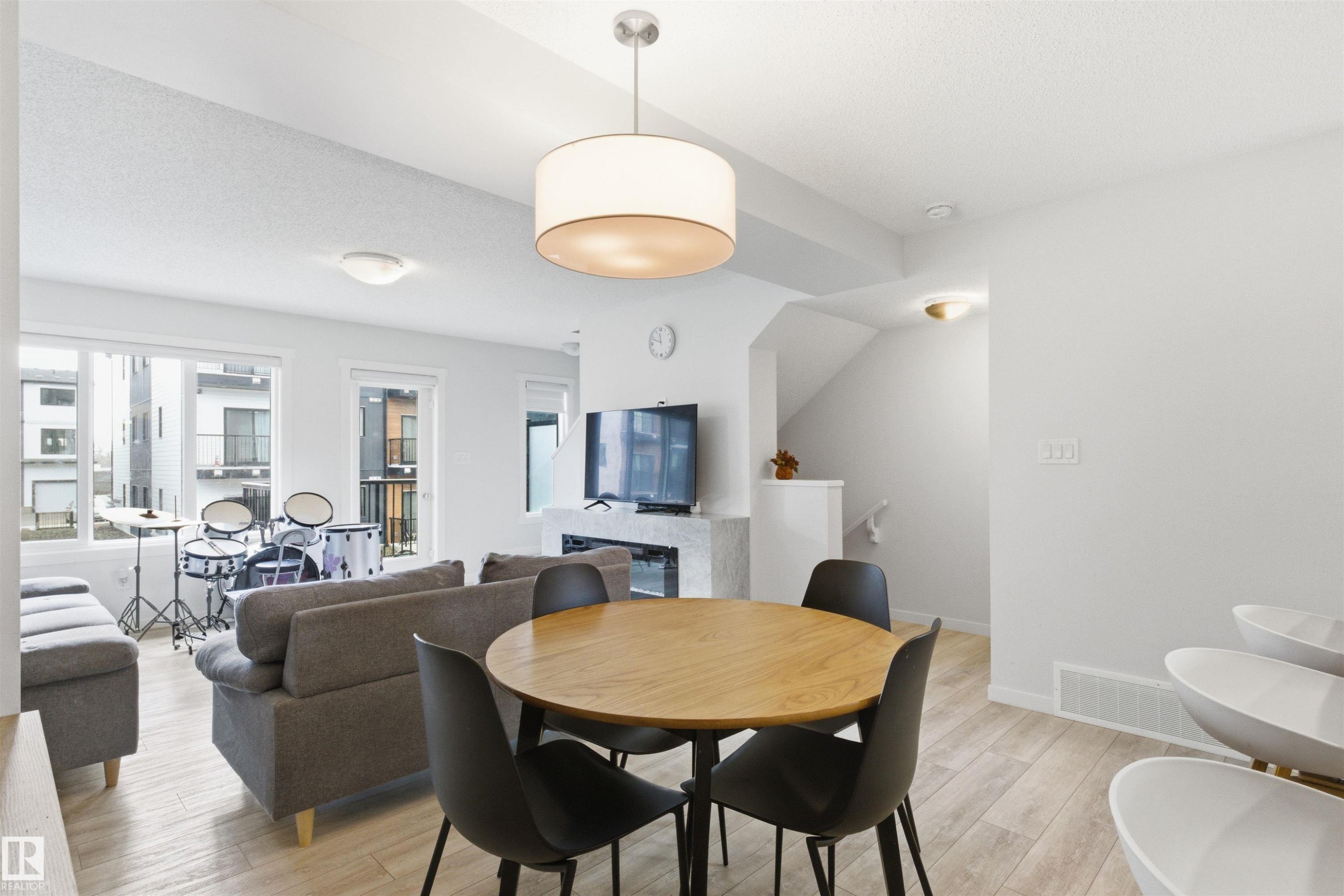 Open-concept living space featuring wood-finish flooring, a modern fireplace, multiple windows for ample natural light, and a contemporary drum pendant light fixture - 9 850 Secord Boulevard, Edmonton, AB - Indoor Photo Showing Dining Room