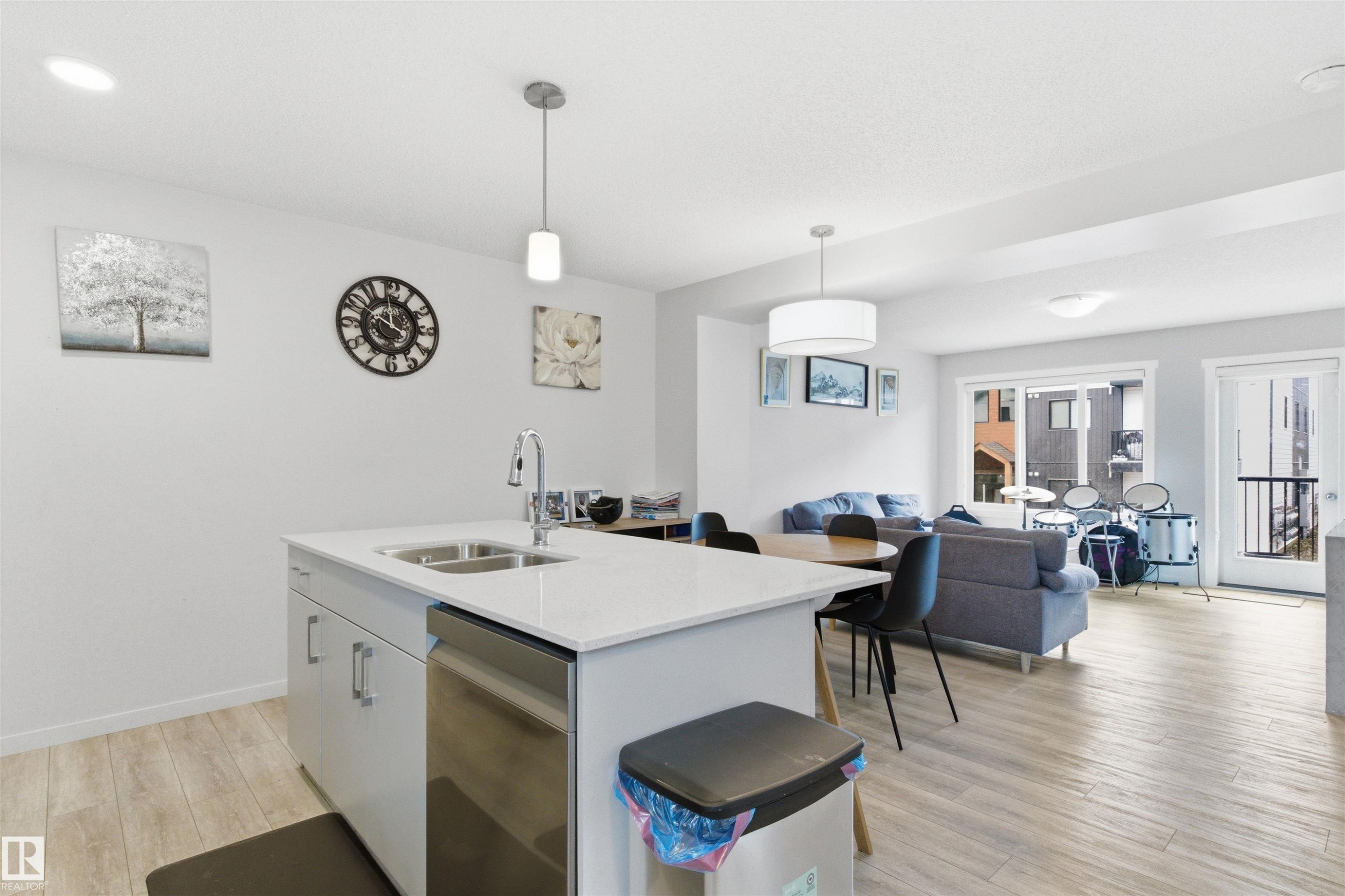 Open-concept living space featuring a kitchen island with dual basin sink and stainless steel dishwasher, wood-finish flooring, recessed lighting, and a sliding glass door leading to a balcony - 9 850 Secord Boulevard, Edmonton, AB - Indoor