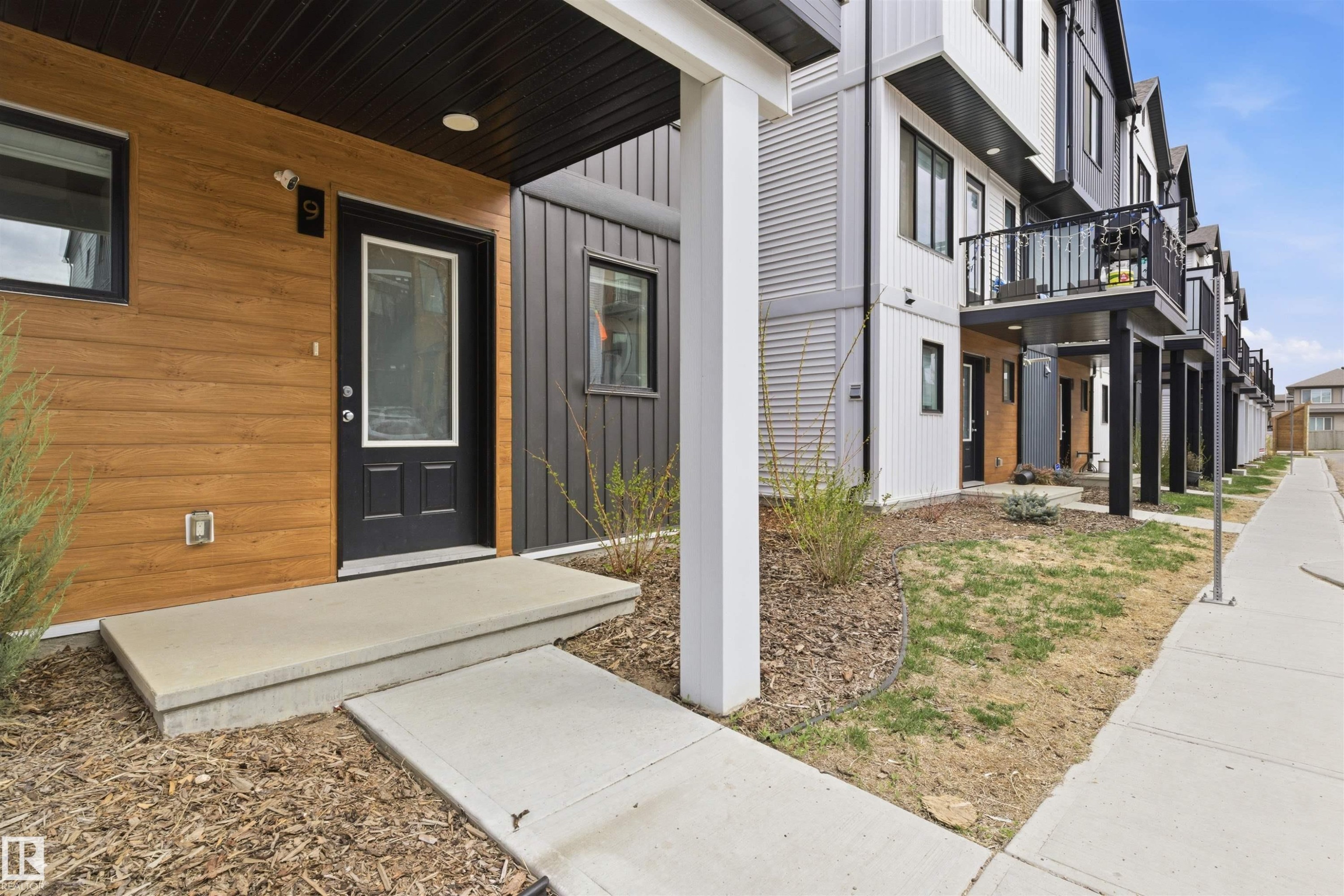 Modern townhome exterior featuring wood-look paneling, dark vertical siding, and a black front door with glass insert - 9 850 Secord Boulevard, Edmonton, AB - Outdoor With Exterior