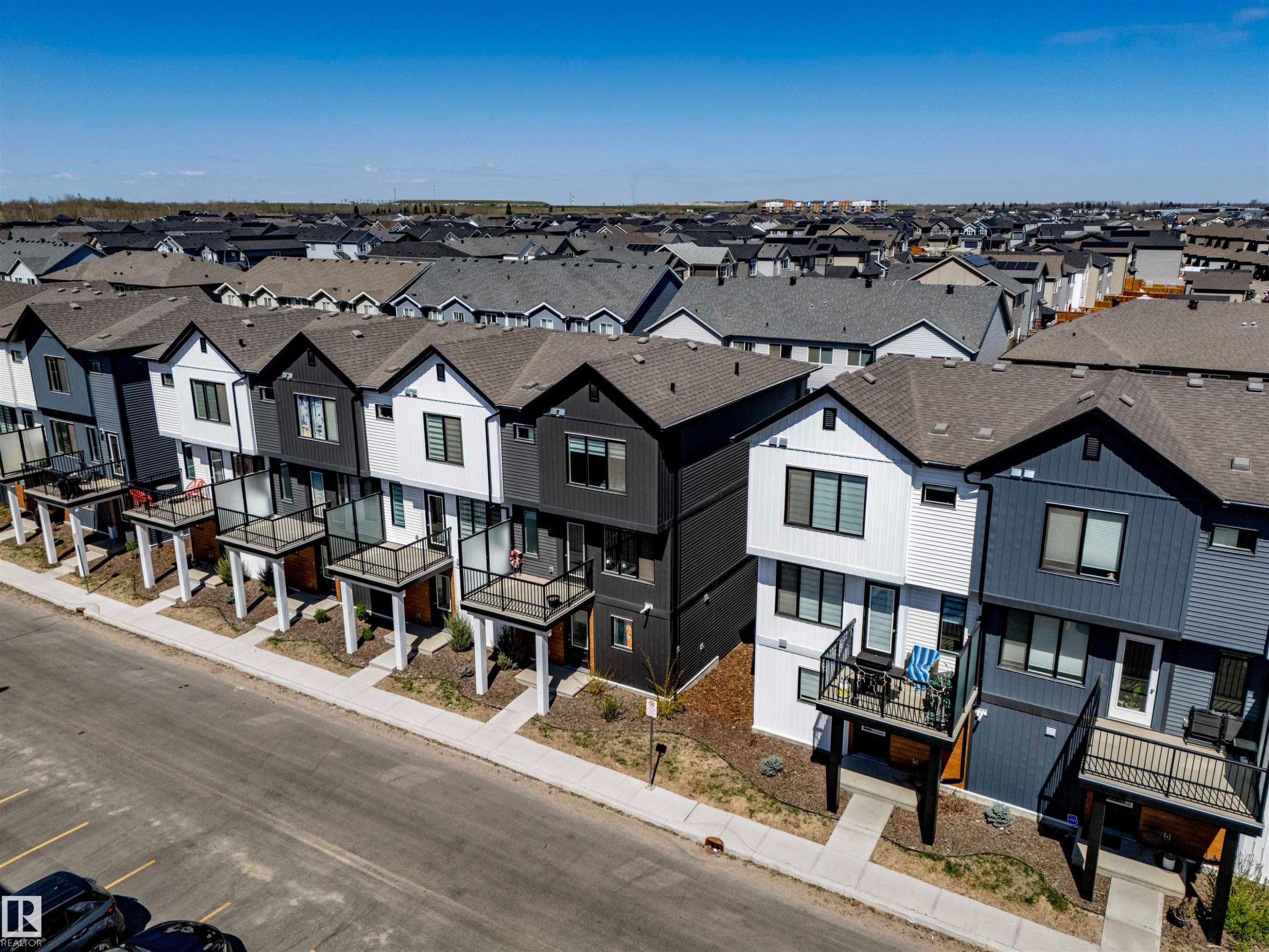Modern townhome exteriors featuring contrasting dark and light siding, multiple balconies with glass railings, and a consistent architectural style - 9 850 Secord Boulevard, Edmonton, AB - Outdoor With Facade
