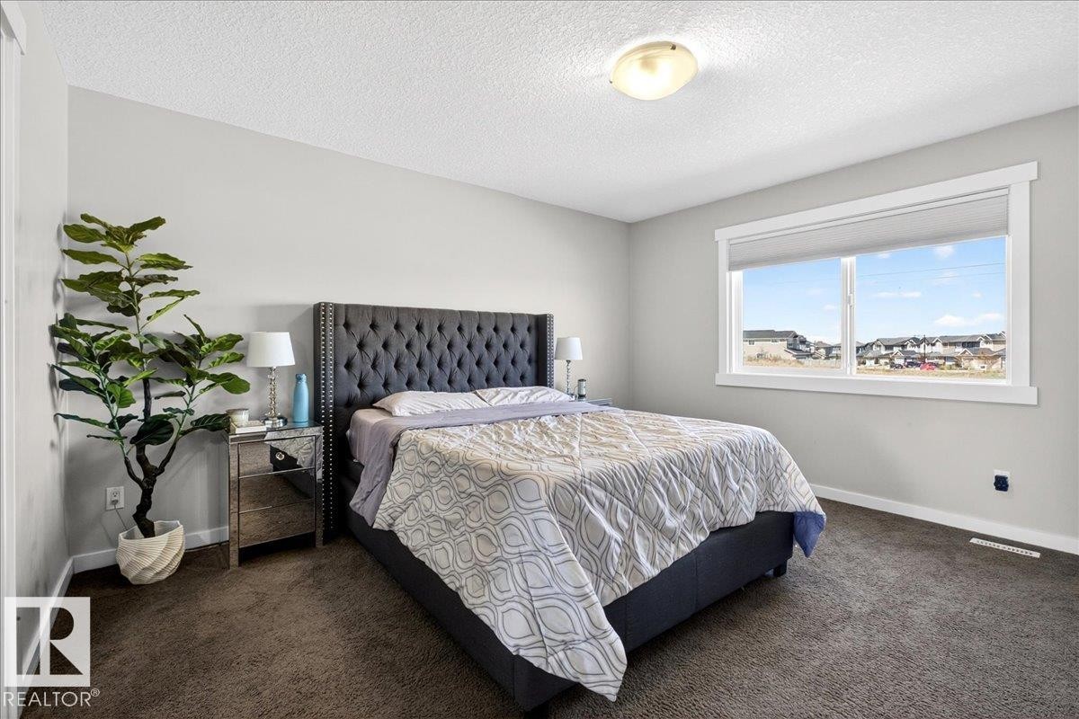 Spacious room featuring neutral painted walls, dark textured carpet, and a large window with white trim - 3936 Claxton Loop, Edmonton, AB - Indoor Photo Showing Bedroom