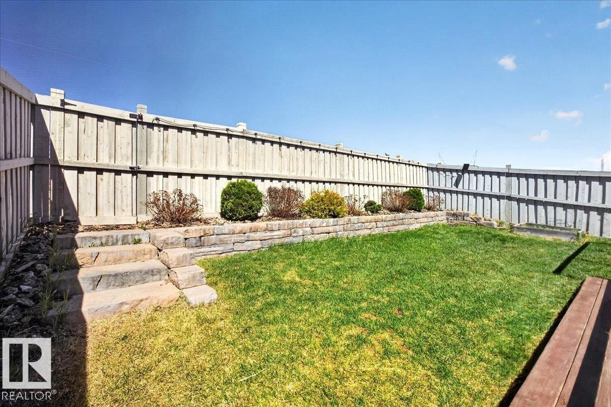 Fenced backyard featuring a tiered retaining wall, stone steps, landscaped garden beds with shrubs, and a grassy lawn - 3936 Claxton Loop, Edmonton, AB - Outdoor