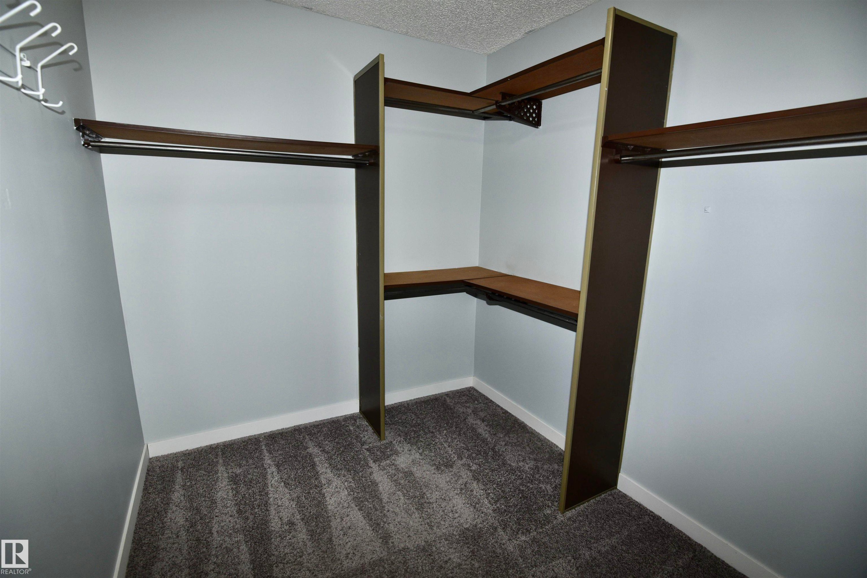 Custom closet system featuring multiple wood-finish shelves and integrated hanging rods - 21 10160 119 Street Nw, Edmonton, AB